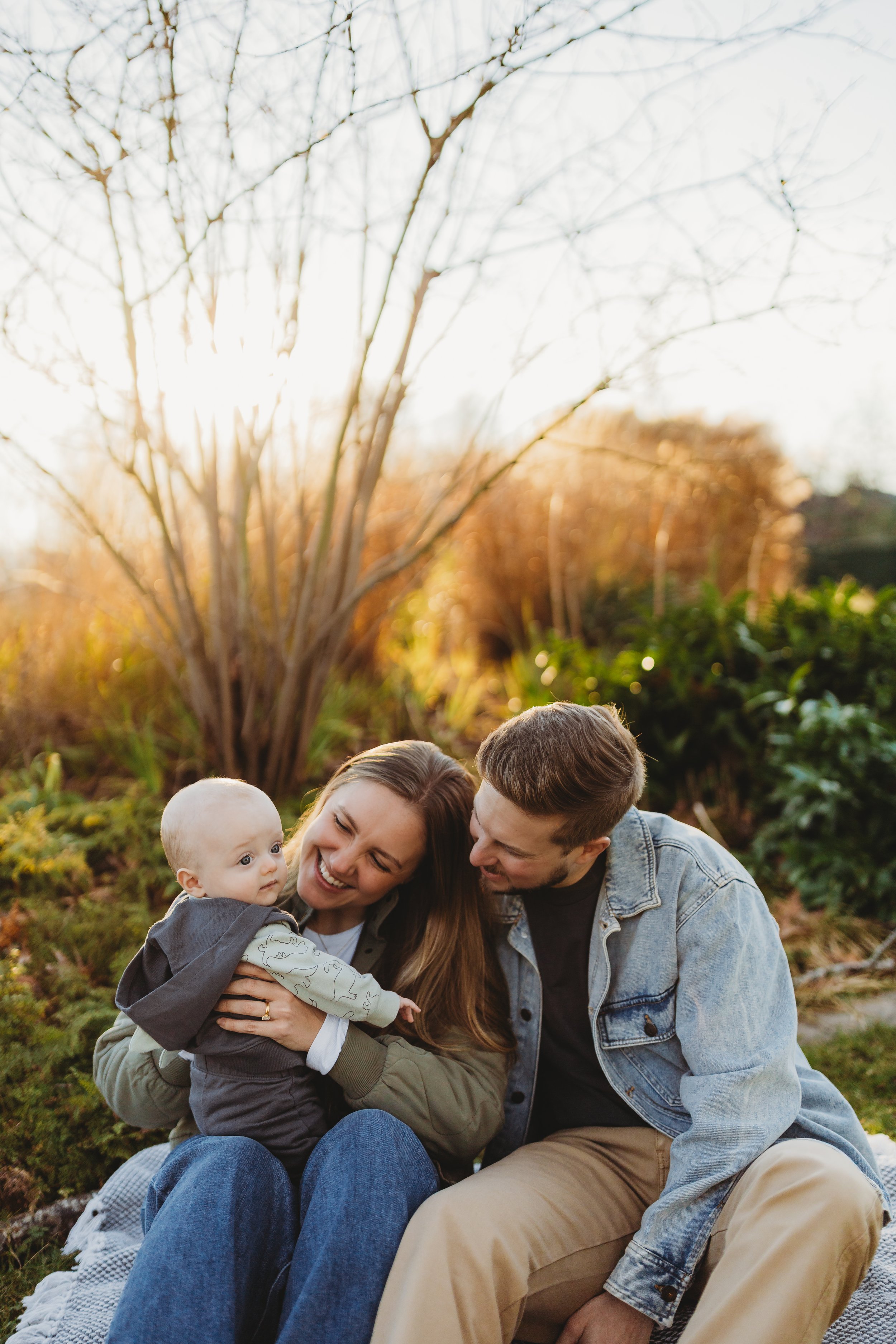 onesie-seattle-family-photographer.jpg	Parents smiling at baby in dinosaur-print onesie at golden hour, Seattle family photographer