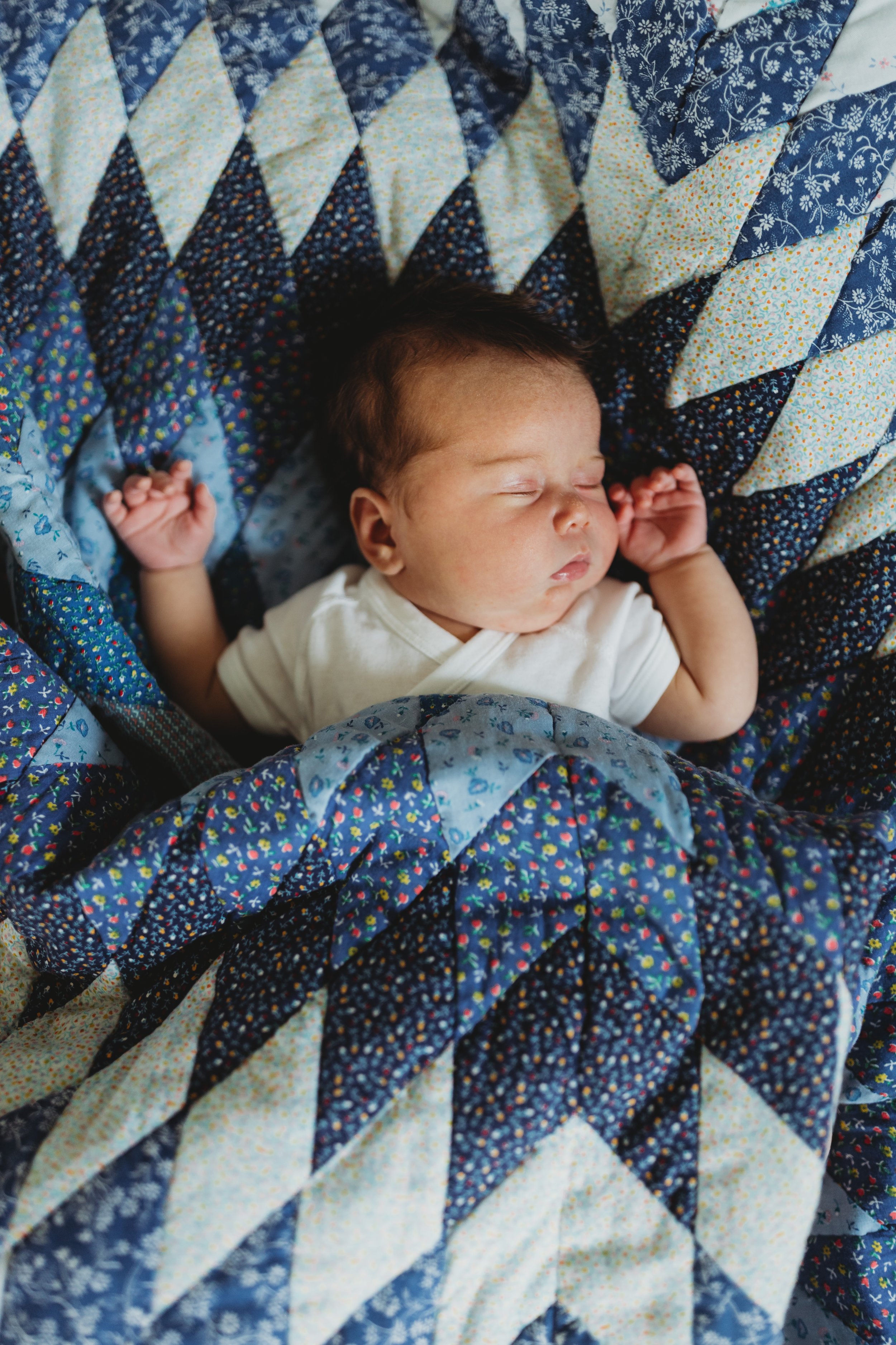 Sleeping newborn swaddled in a quilt during a Seattle in-home lifestyle newborn session, wearing a simple white onesie.