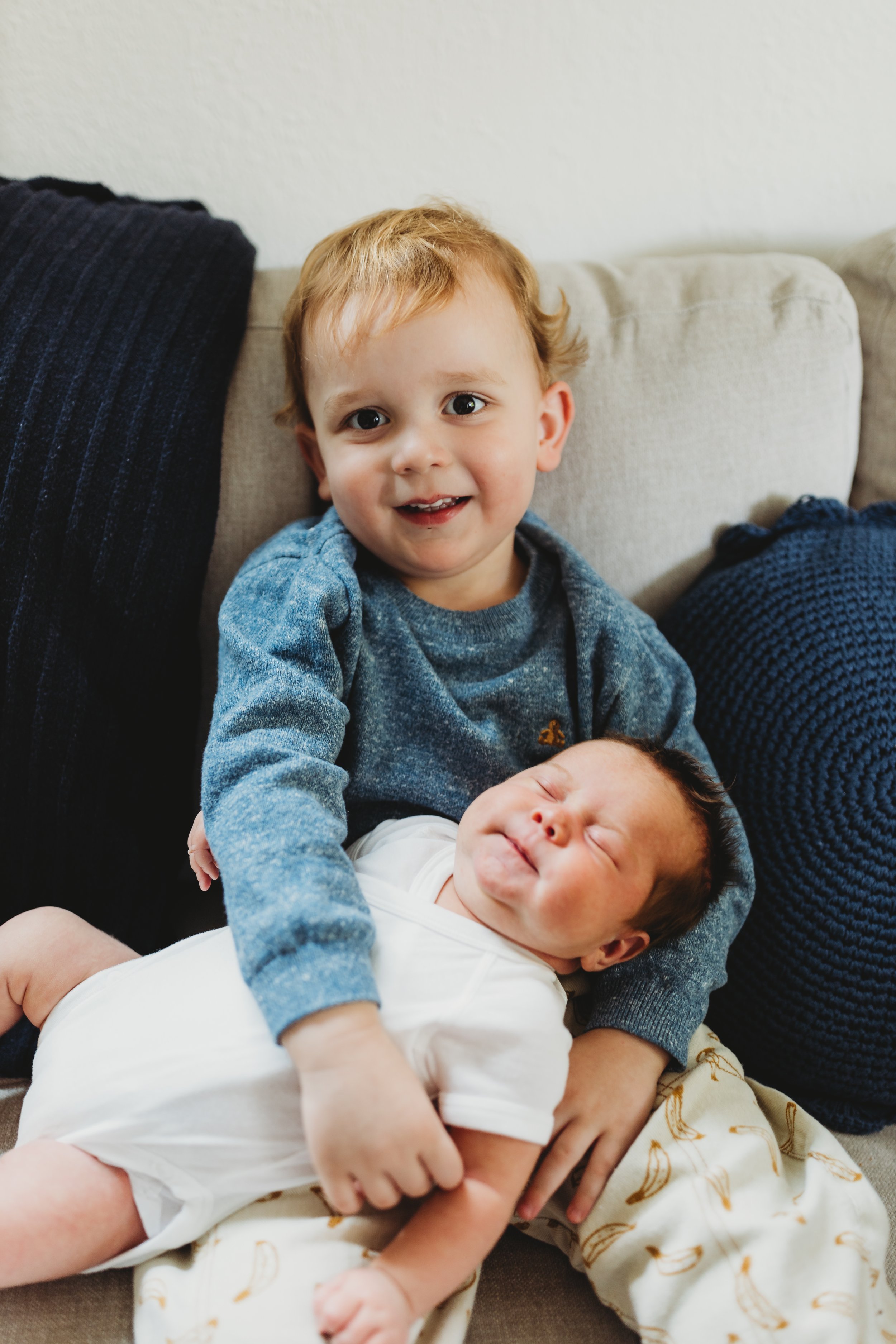 Toddler holding newborn sibling on a couch during an in-home family newborn photography session in Seattle.