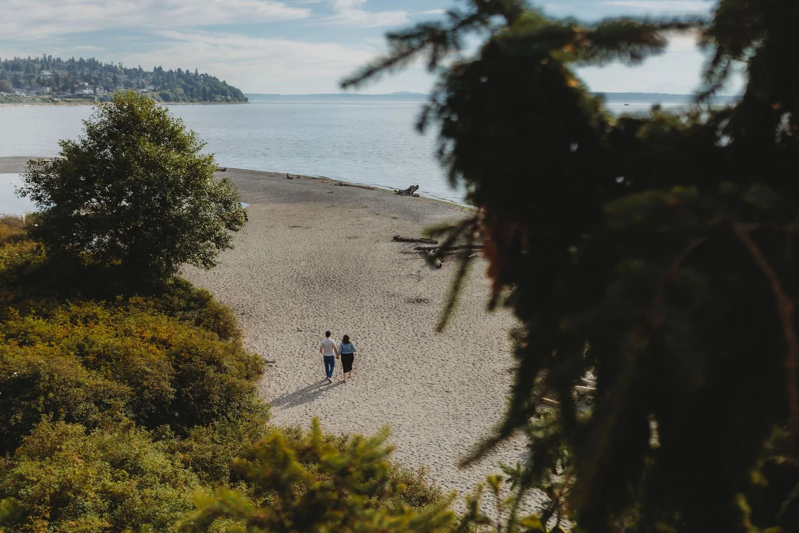Expecting couple walking along the beach during a natural light maternity photo session at Carkeek Park in Seattle.