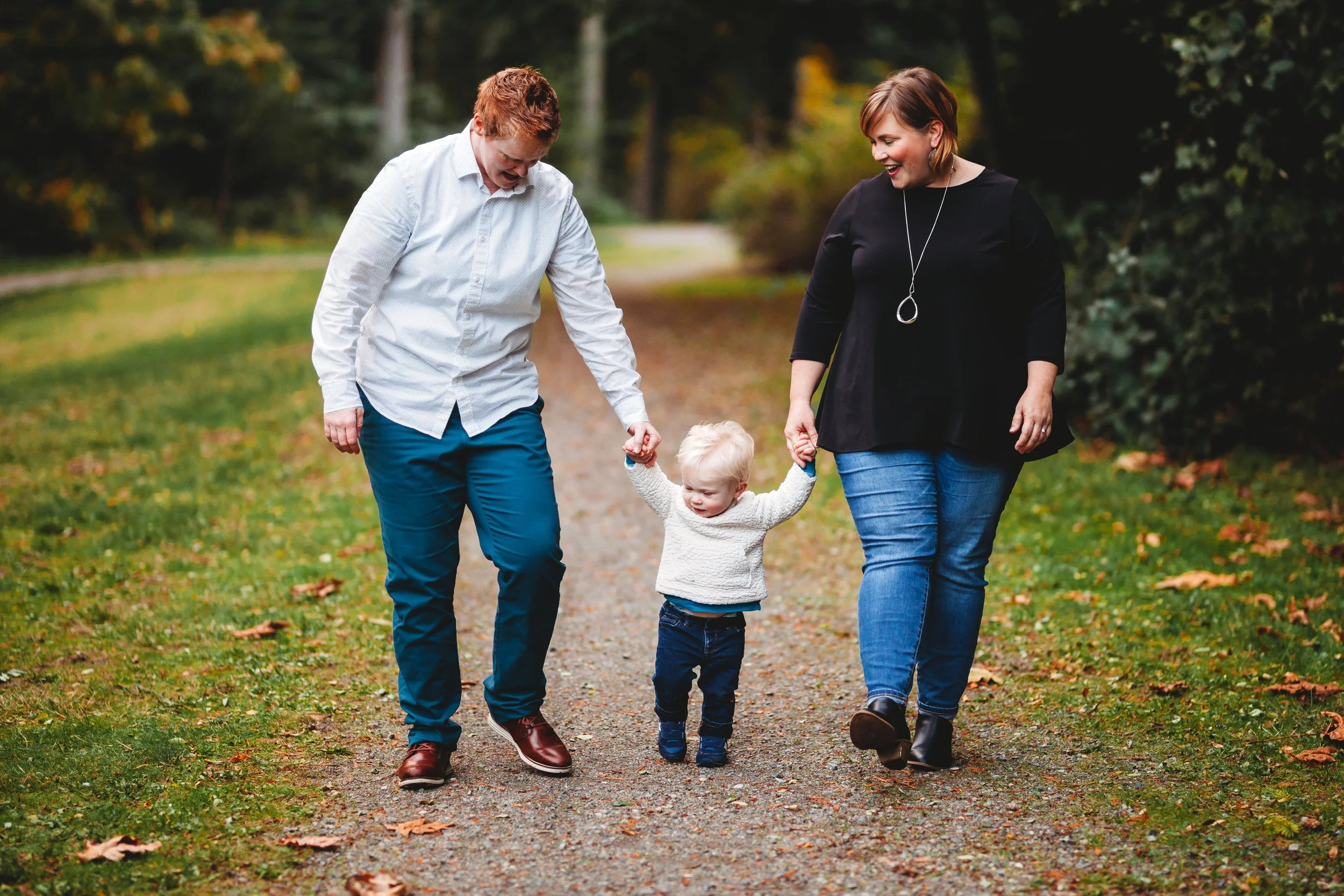 Queer couple walking with their toddler along a wooded path at Boeing Creek Park during a relaxed natural light family photo session.