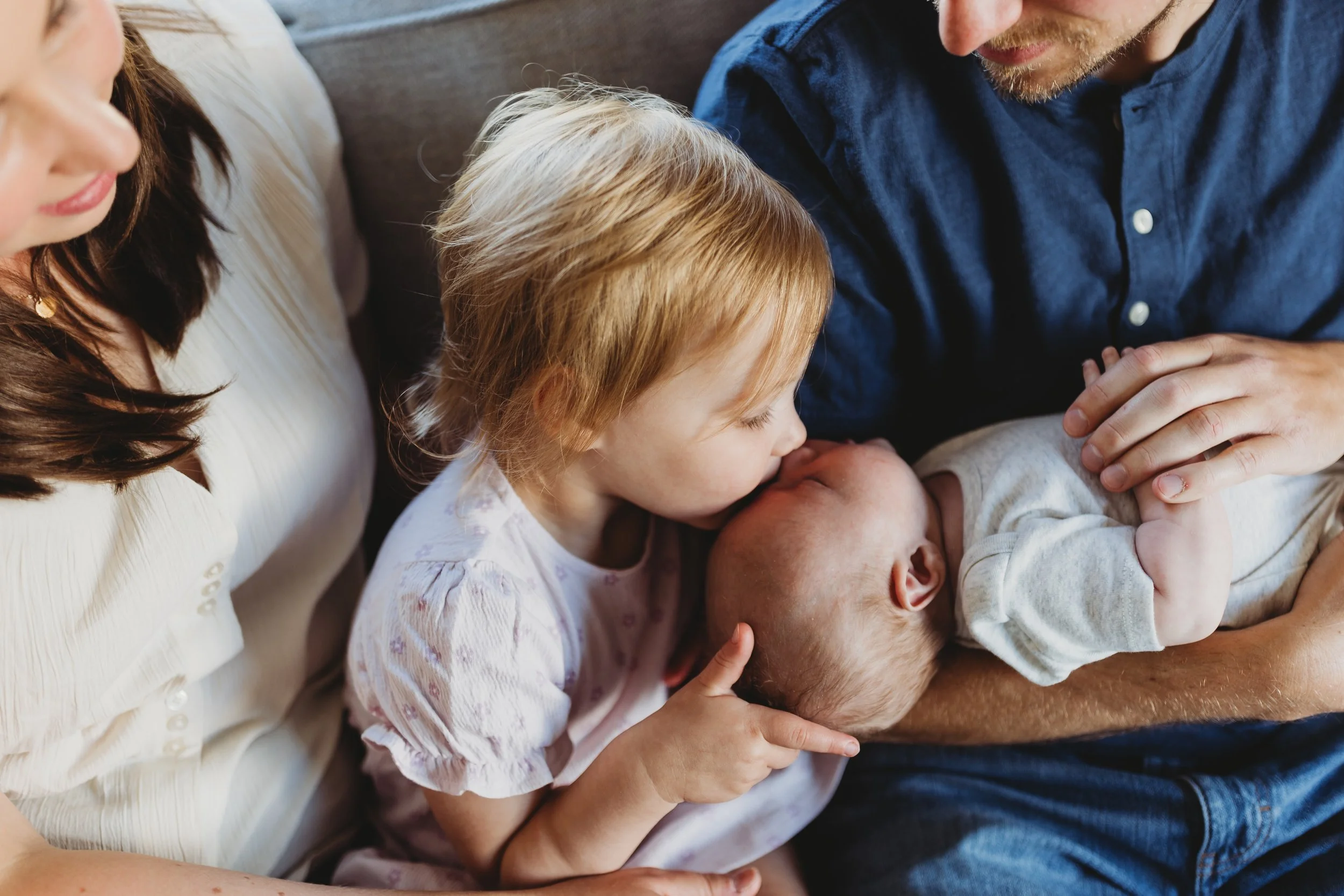 Toddler kissing newborn sibling during in-home lifestyle newborn photo session in Seattle