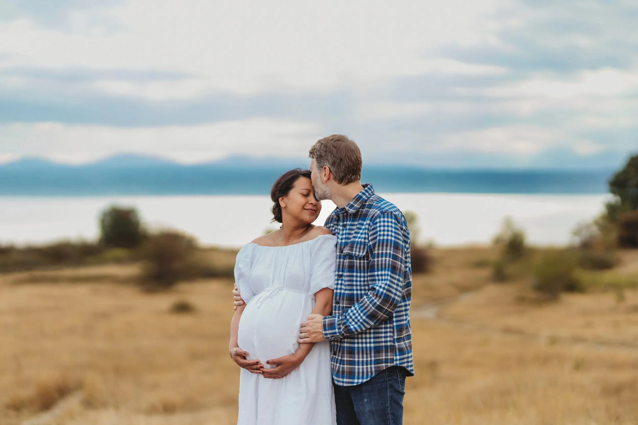 Expecting couple sharing a quiet moment during a maternity photo session at Discovery Park in Seattle with soft natural light and open meadow views.