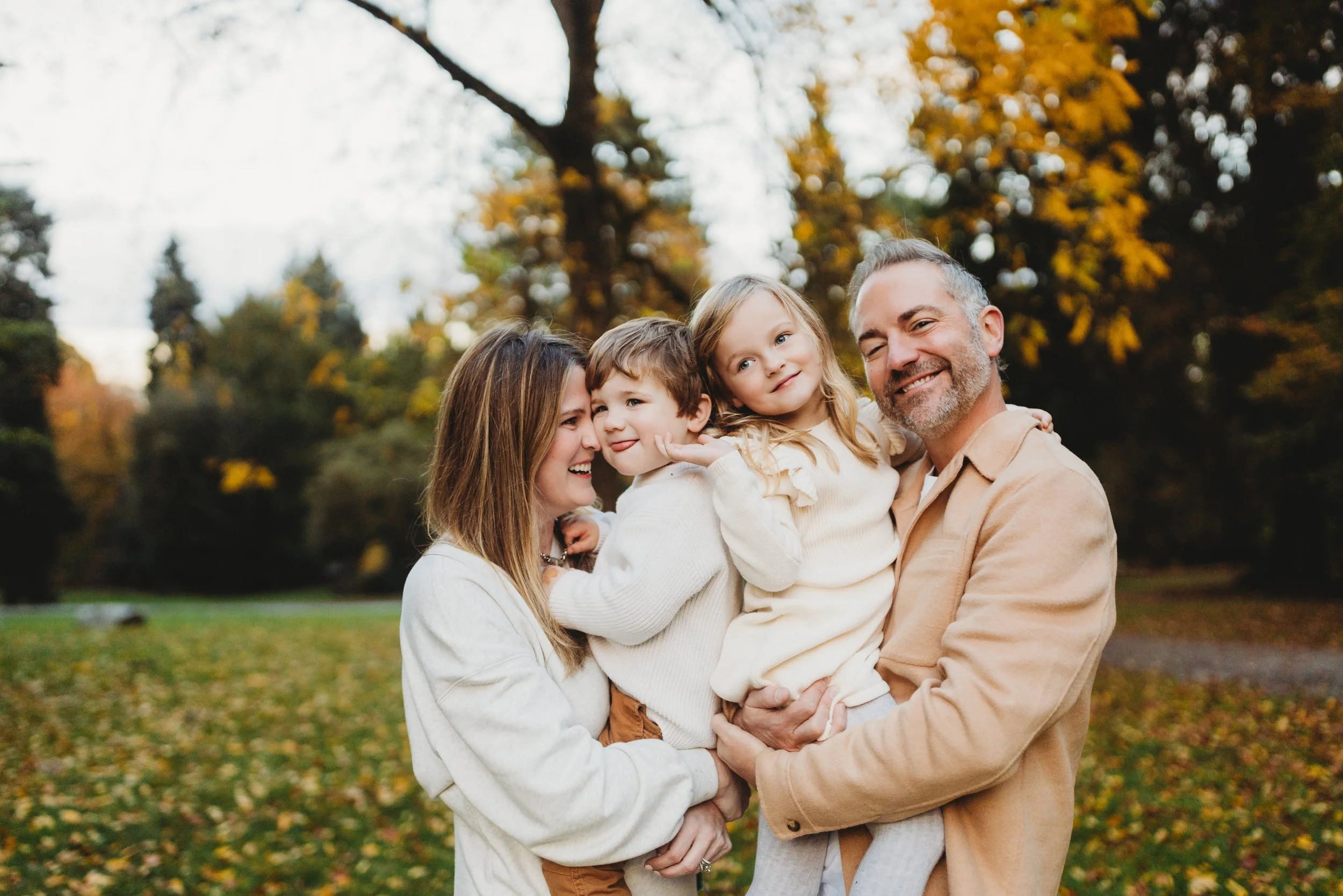 Family of four cuddling together during a fall photo session at Volunteer Park in Seattle, surrounded by autumn foliage
