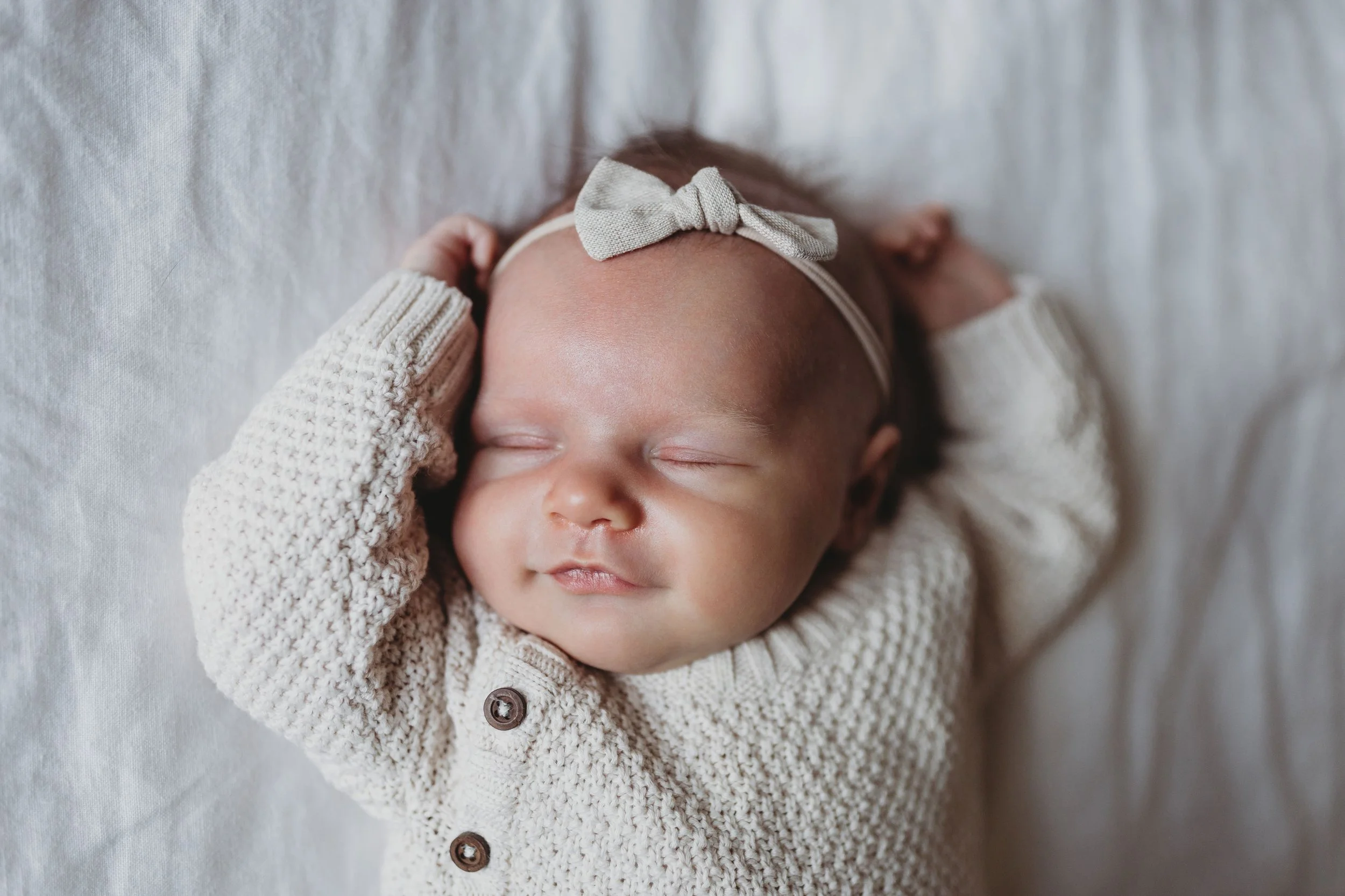 Sleeping newborn baby girl in cream knit cardigan and bow headband, photographed during an in-home newborn session in Seattle