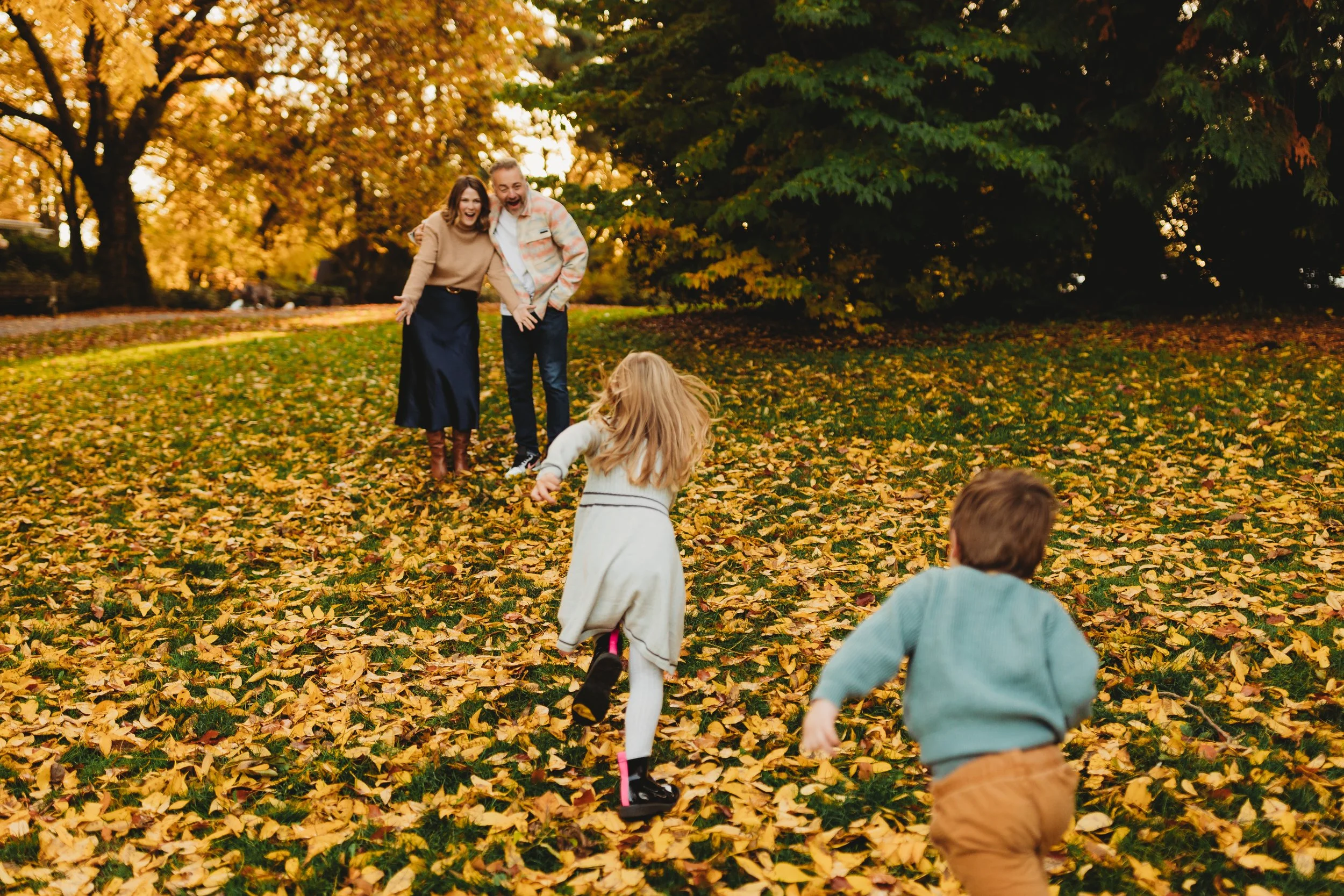 Kids running through fall leaves toward laughing parents, Volunteer Park fall mini session, Seattle photographer