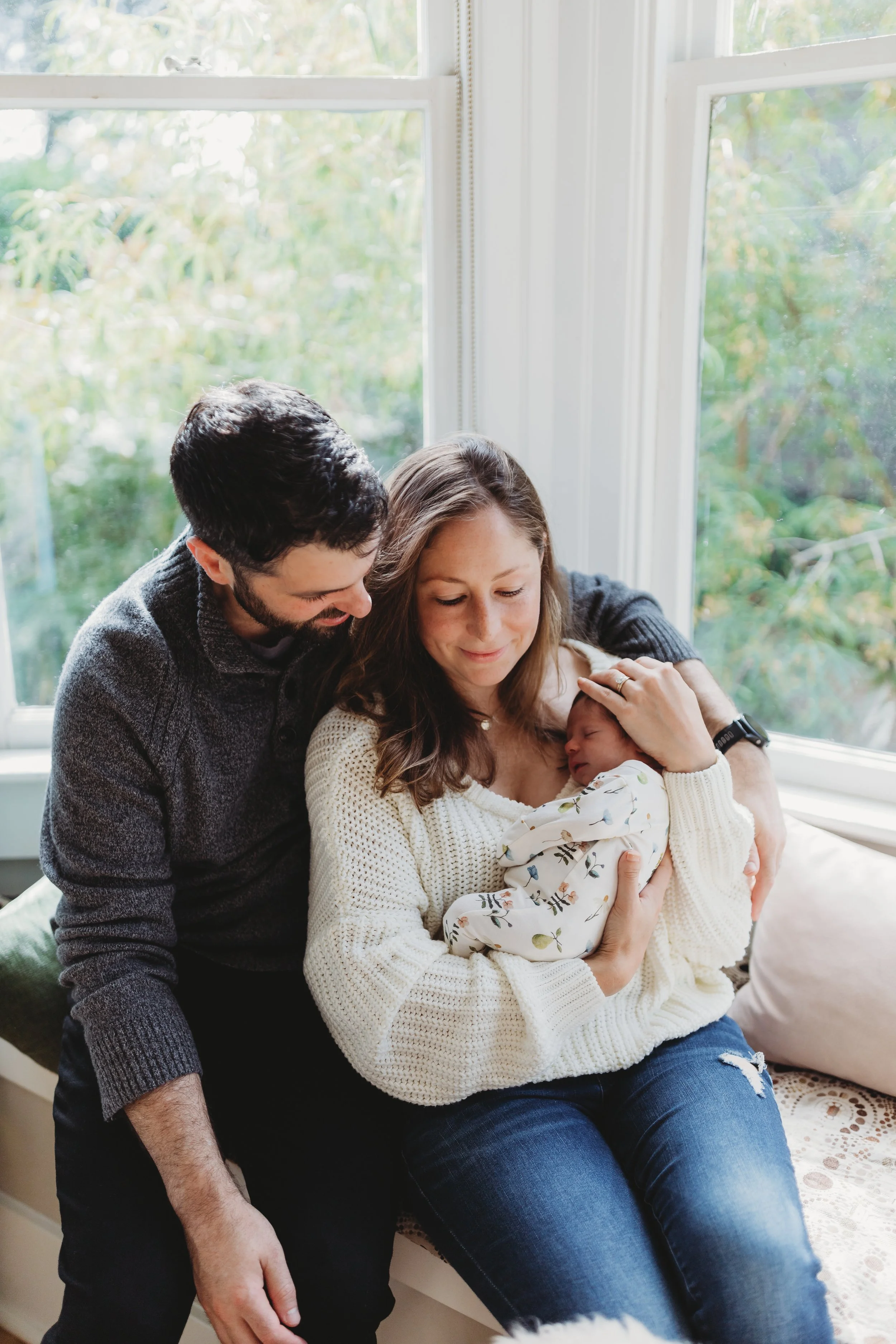 Parents wearing neutral, coordinated outfits while holding their newborn during a Seattle in-home lifestyle newborn session with natural light.