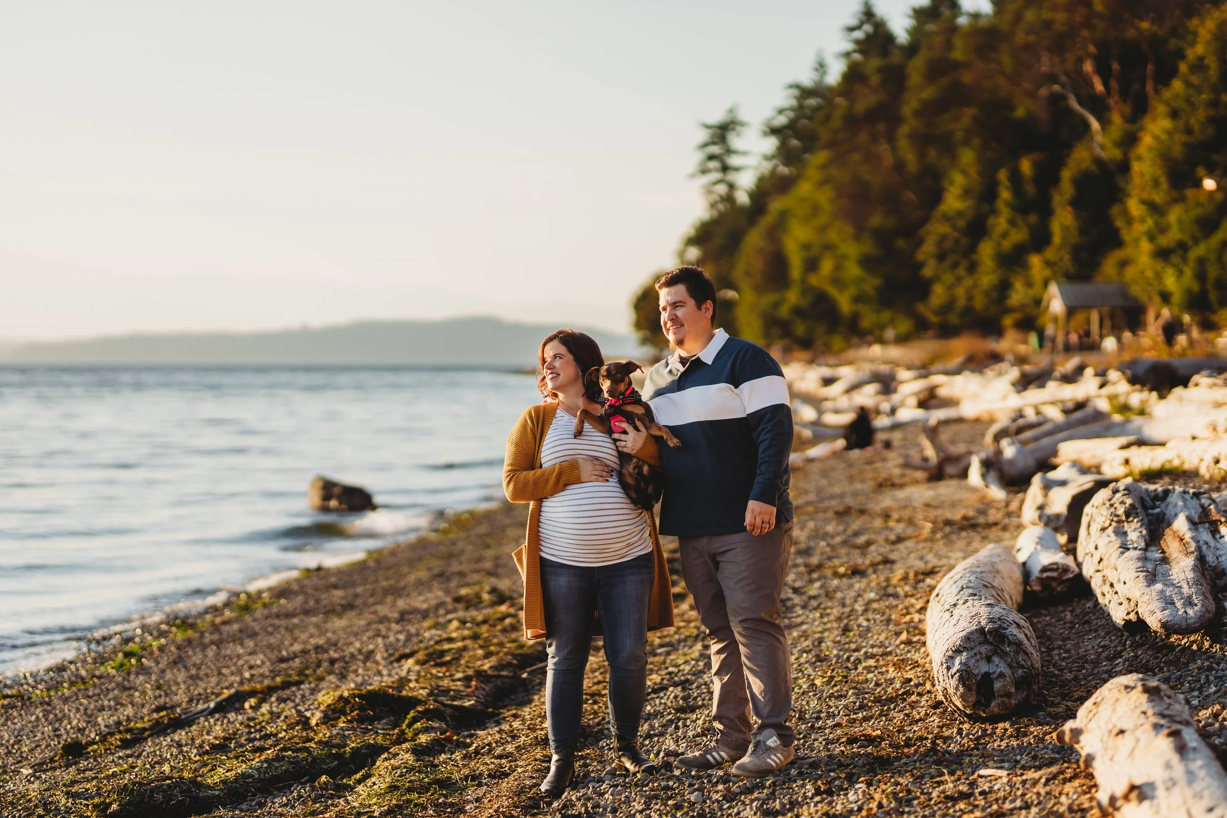 Pregnant couple walking along the beach at Lincoln Park during a maternity photo session in Seattle.