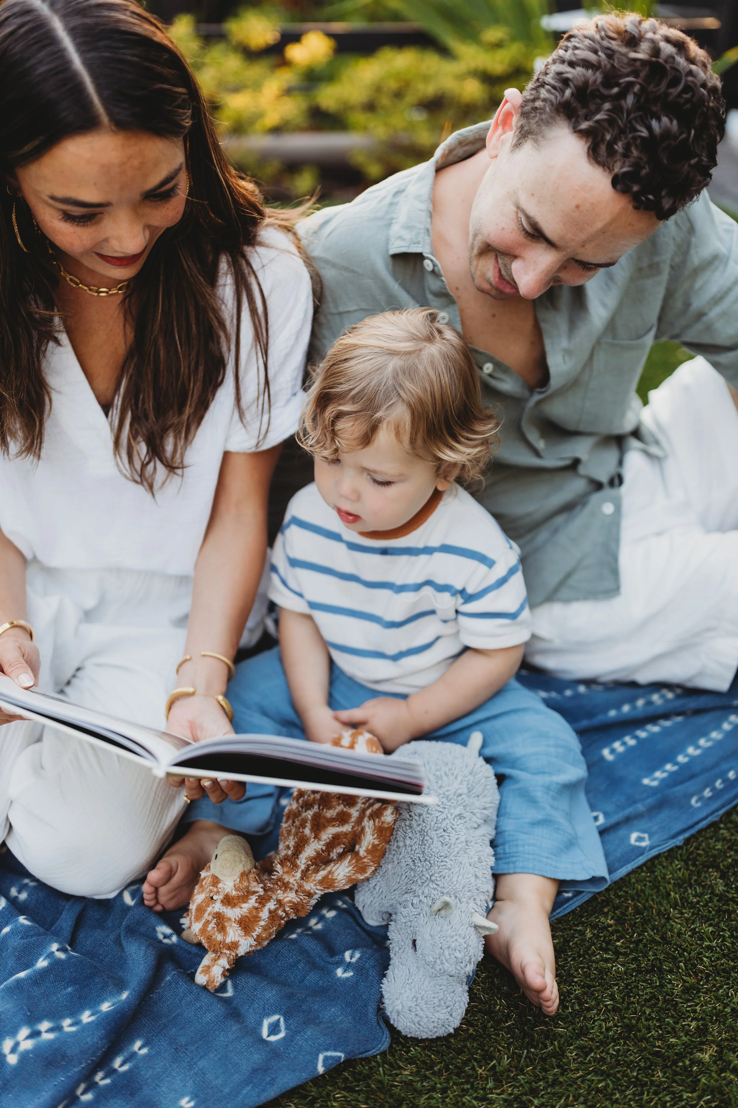 Mom and dad reading a book with their toddler on a blanket outdoors during a relaxed Seattle family mini session