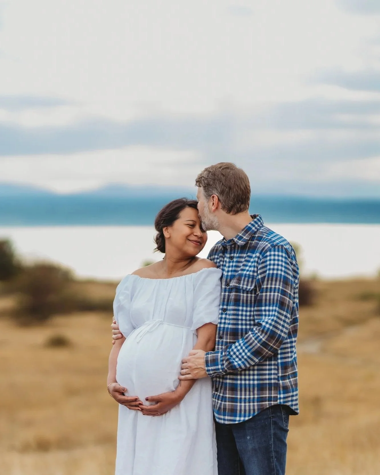Seattle maternity photographer — outdoor maternity session at Discovery Park, couple embracing with Puget Sound in background