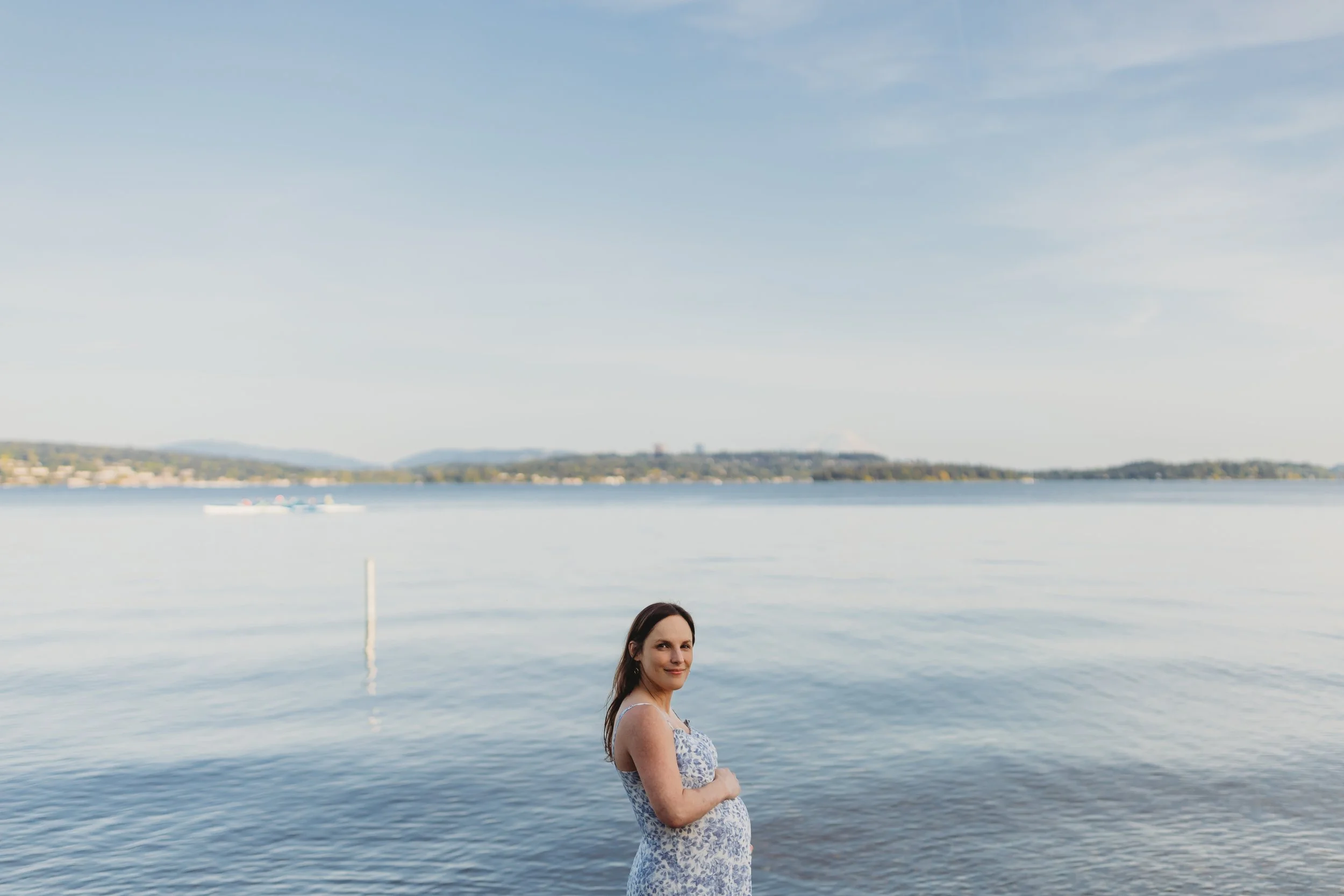 Maternity photo of an expecting mother standing by the water at Magnuson Park in Seattle with Lake Washington in the background.