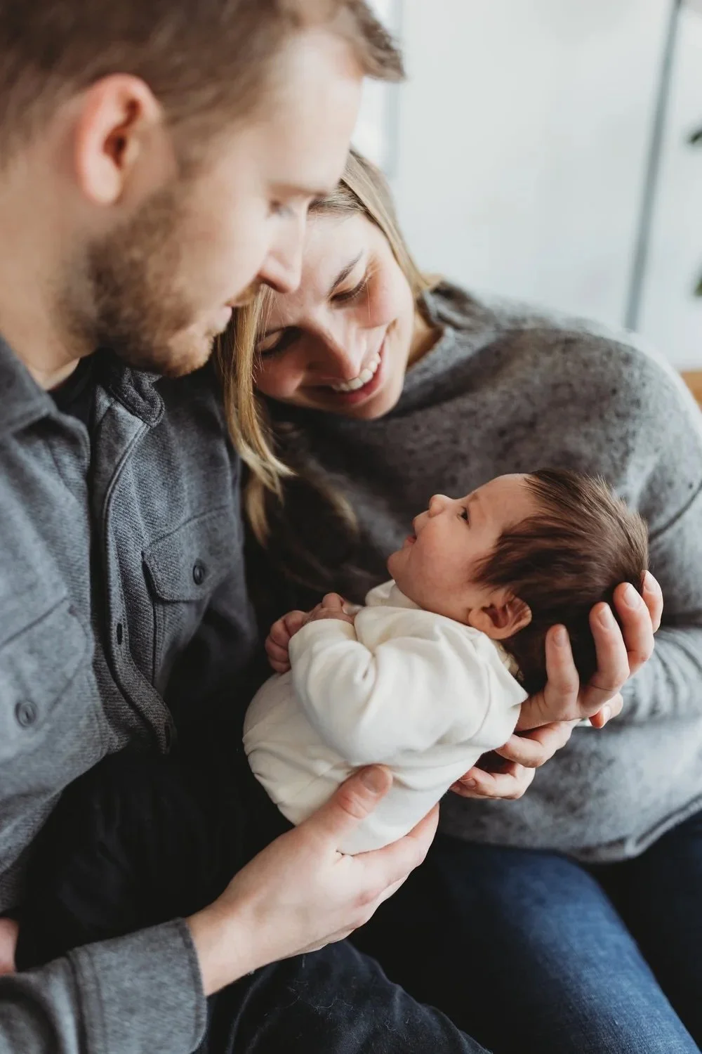Parents holding their newborn during a relaxed in-home newborn photo session in Seattle, wearing soft neutral layers in natural light.