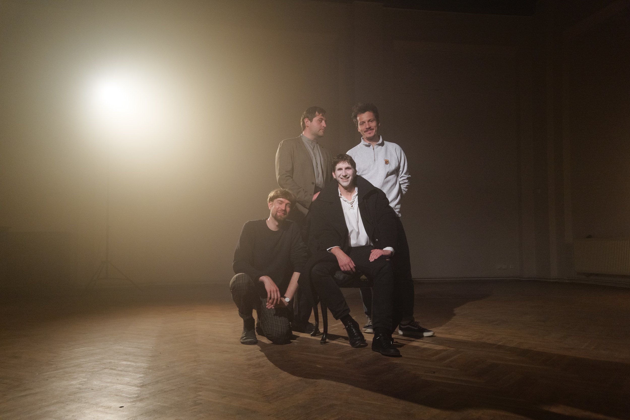 An expressive group photo with four people in a minimalist space. The soft lighting and vintage atmosphere give the shot a particular drama and aesthetic.
