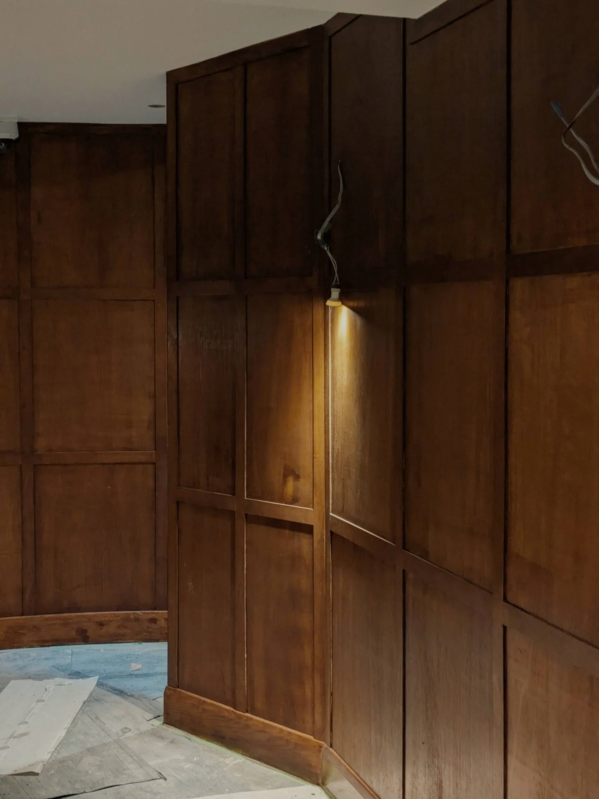 Fleet Tavern interior refurbishment by Polysmiths — heritage timber frame with antique clock as bar backdrop, deep green surfaces, stained dark timber panelling and brass wall lights, Hampstead NW3