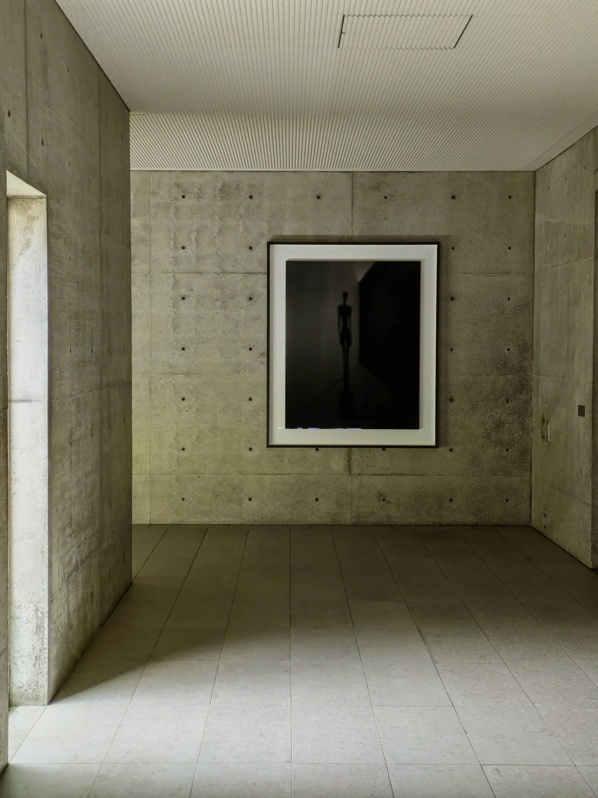 Chichu Art Museum interior, zenithal light on concrete Interior gallery of Tadao Ando's Chichu Art Museum: raw board-formed concrete surfaces lit by zenithal natural light from above, shadow arcs moving slowly