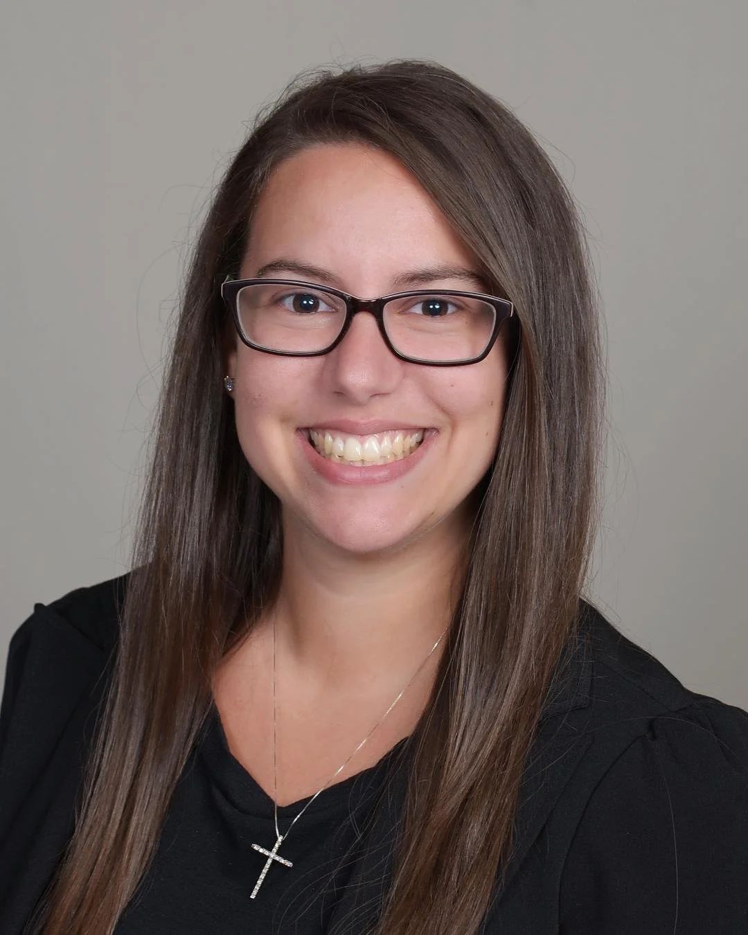 Headshot of Katlyn Von Glahn, LMSW, therapist at Upstate Counseling, smiling with long straight brown hair, wearing glasses, a black top, and a cross necklace against a plain light background.