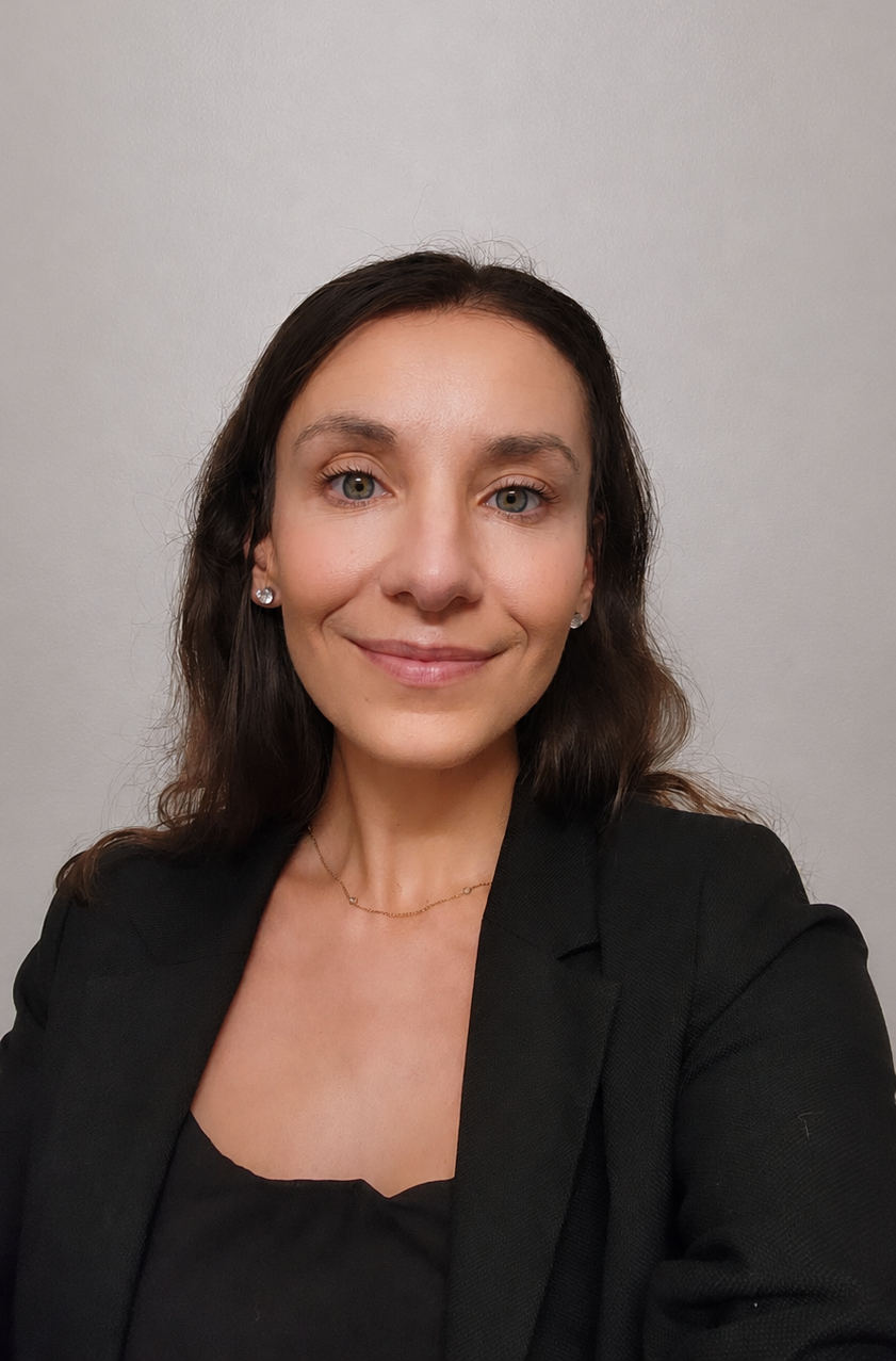 Headshot of Antonija Pjetri, LCSW, therapist at Upstate Counseling, smiling with shoulder-length dark brown hair, wearing a black blazer, stud earrings, and a delicate necklace against a plain light background.