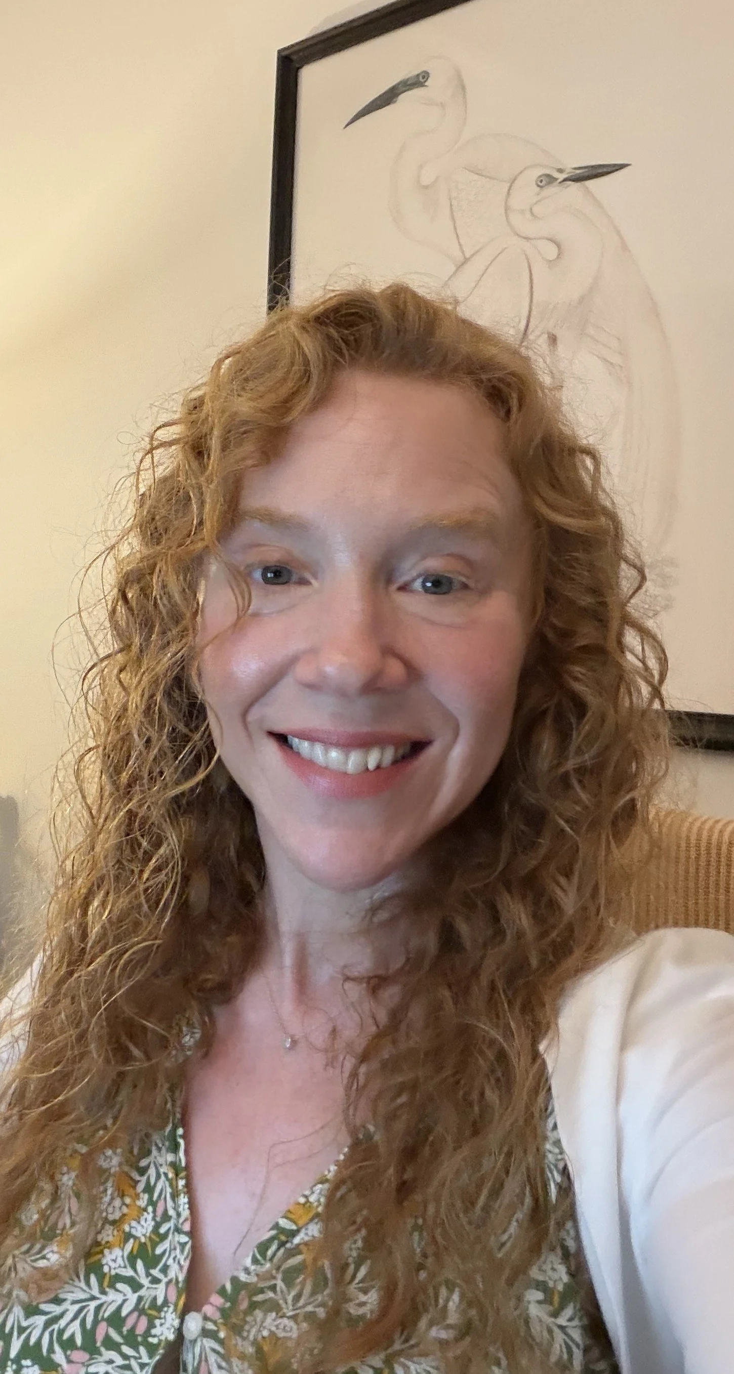 Headshot of Madeline Kennedy, LMSW, therapist at Upstate Counseling, smiling with long curly strawberry-blonde hair, wearing a light-colored cardigan and delicate necklace, photographed indoors against a softly lit neutral background.