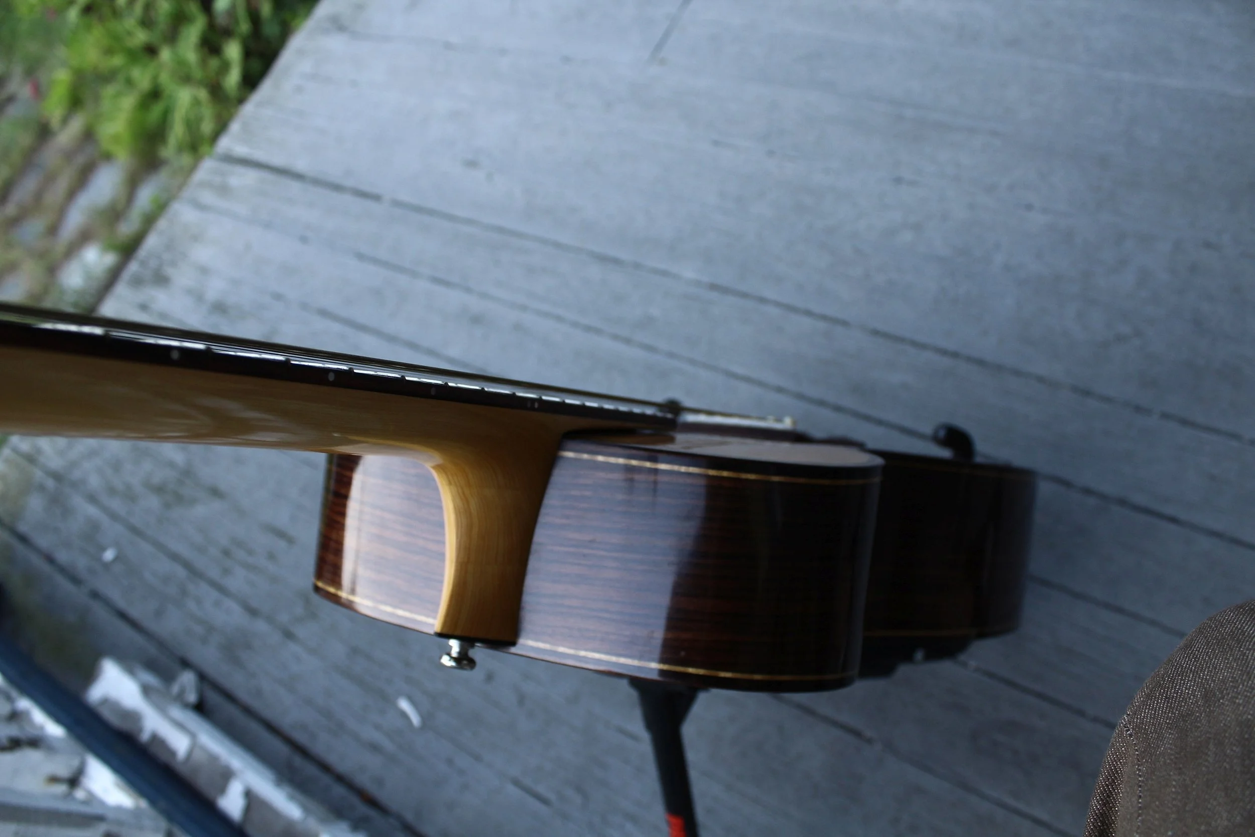a cantilever steel string acoustic guitar stand on a porch showing off the floating fretboard extension and incidentally the stunning contrast of the indian rosewood sides and binding with the laurel purfling