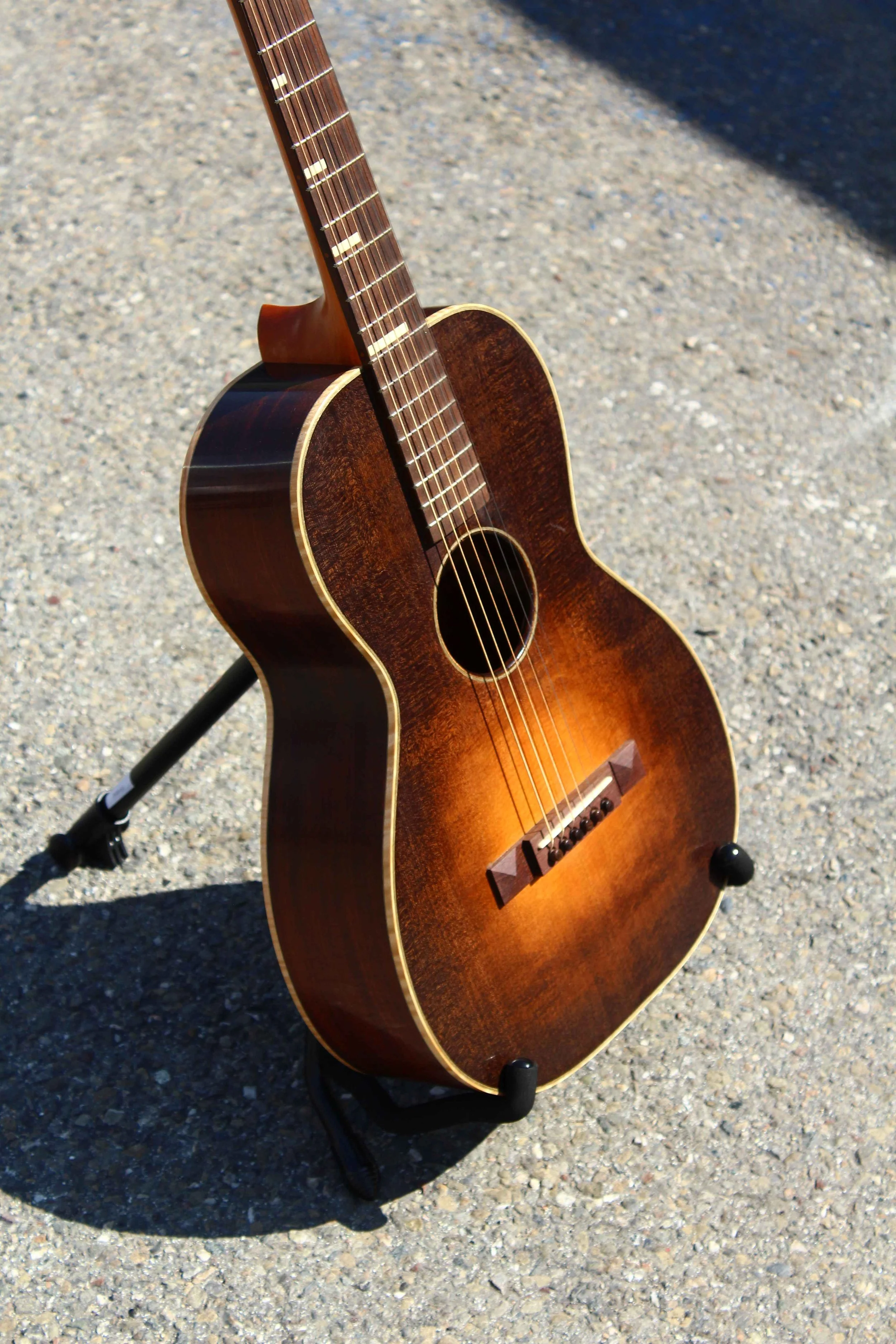 sunburst size 0 acoustic guitar custom made by Queen City Guitars sits on a stand in the sunshine outside of luthier Aaron Foster's former shop in Oakland California
