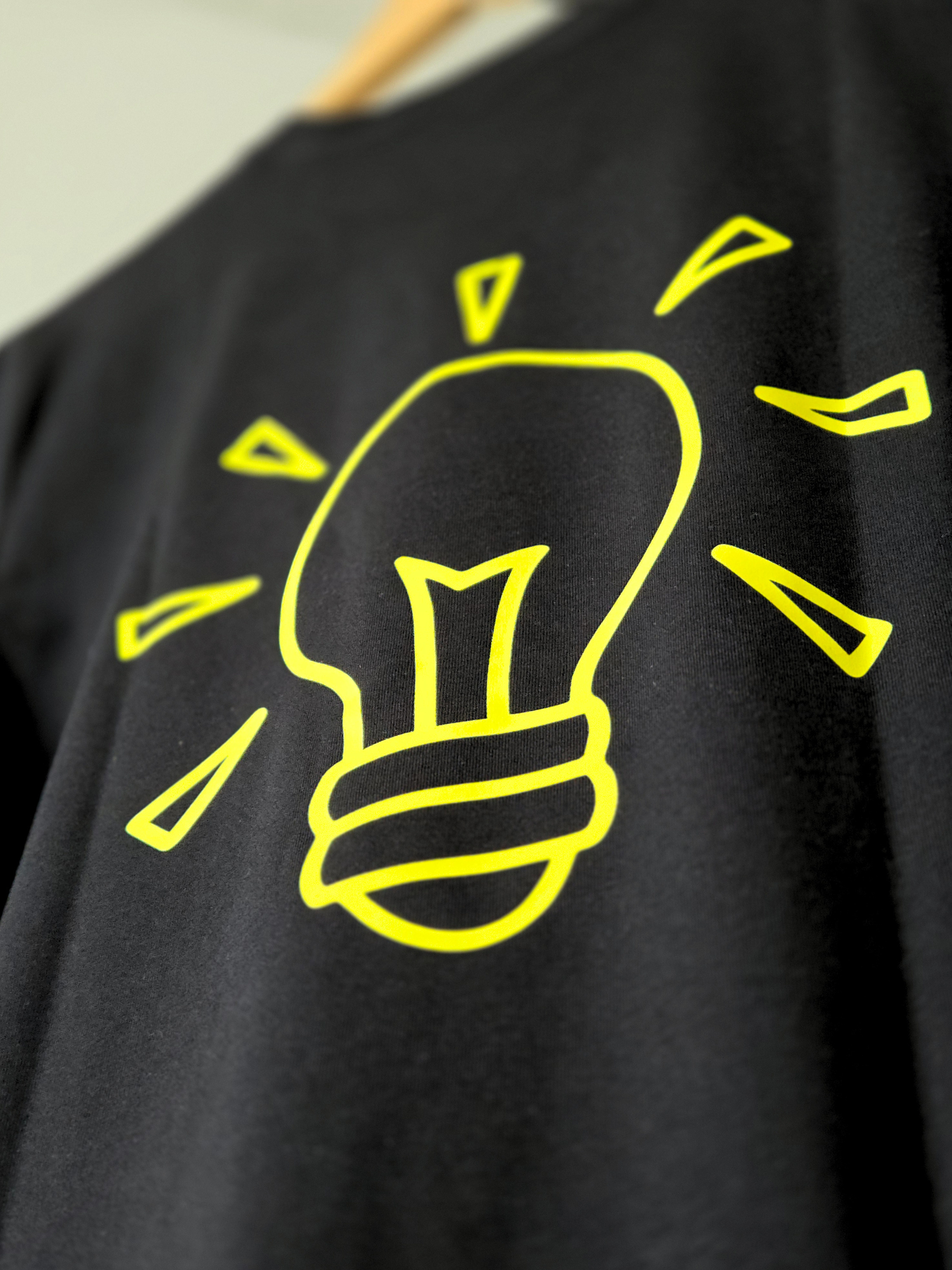 Close-up of a black fabric with a yellow line drawing of a light bulb and emanating light rays.