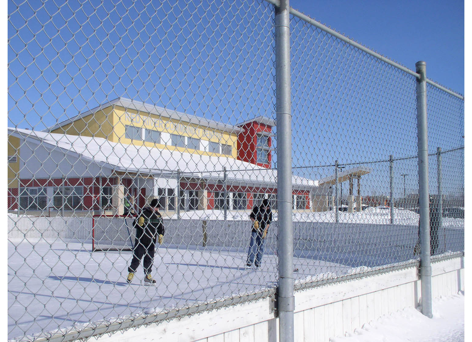  Red River Community Centre, exterior photo of building in winter with kids playing hockey in foreground 