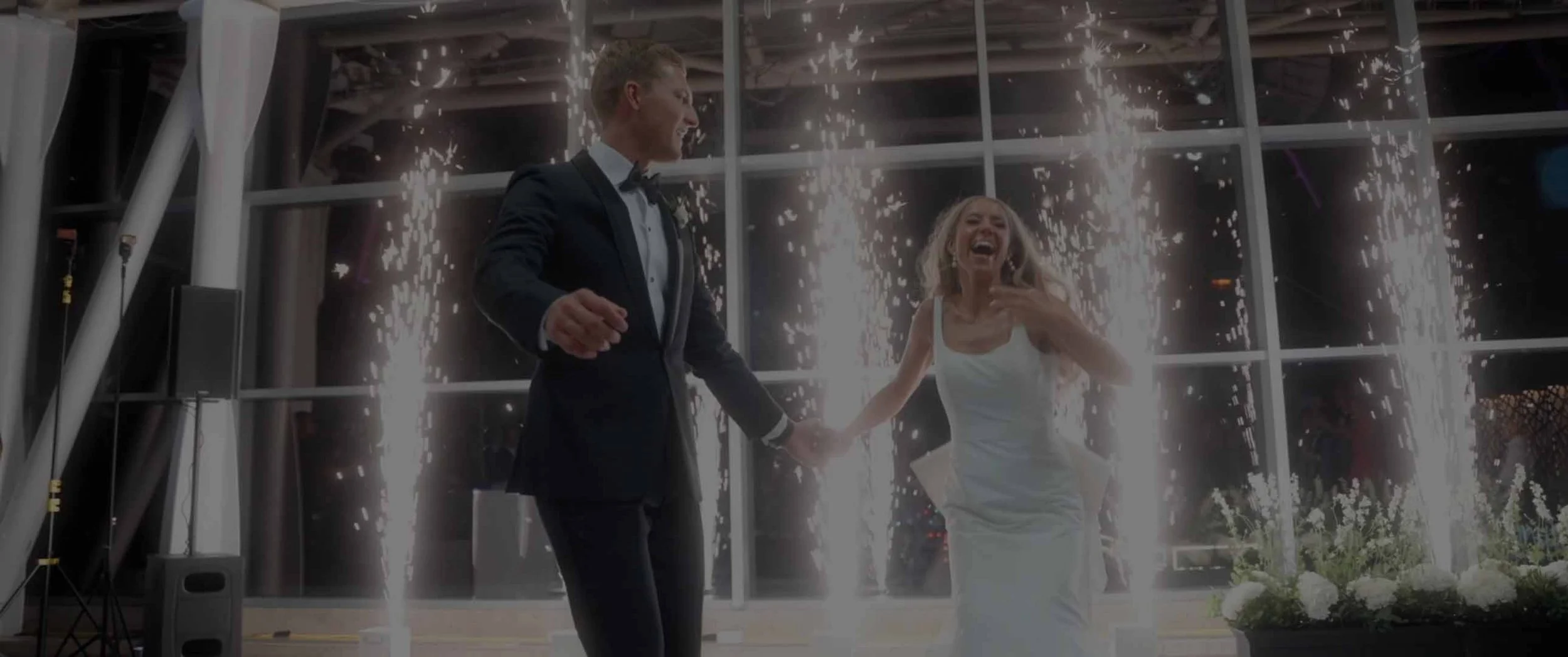 A bride and groom celebrating at their wedding reception with sparklers in the background, holding hands and smiling. Luxury wedding at Arts Garden, Indianapolis
