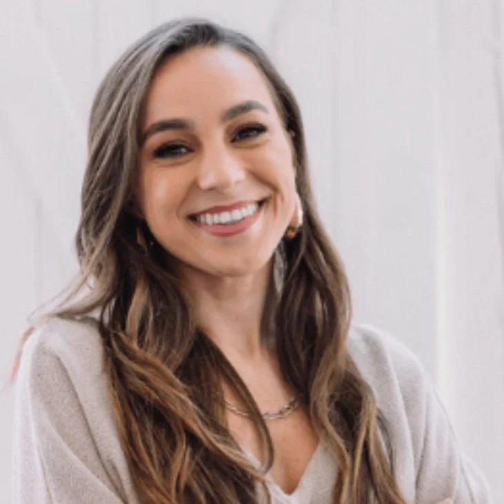 A smiling woman with long brown hair, wearing a light-colored top and earrings. The Sixpence Venue