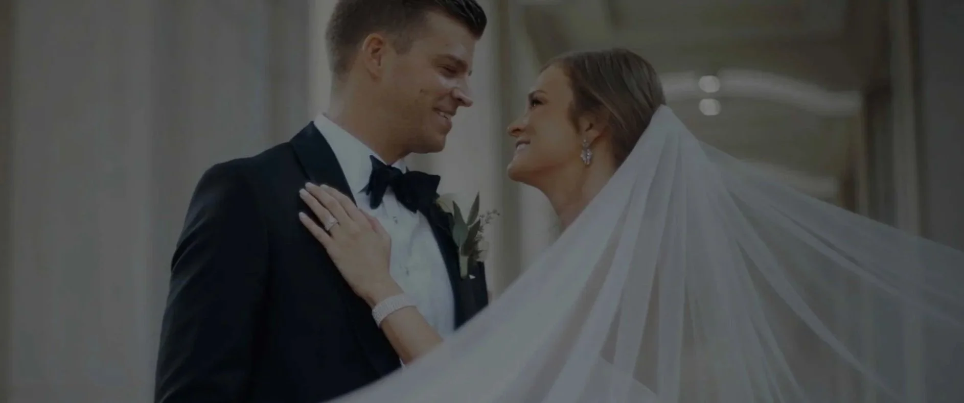 Bride and groom smiling at each other during wedding ceremony, bride wearing white veil and earrings, groom in tuxedo, with a hand on the groom's shoulder, both appear happy and in love. Best wedding videographer in Indianapolis