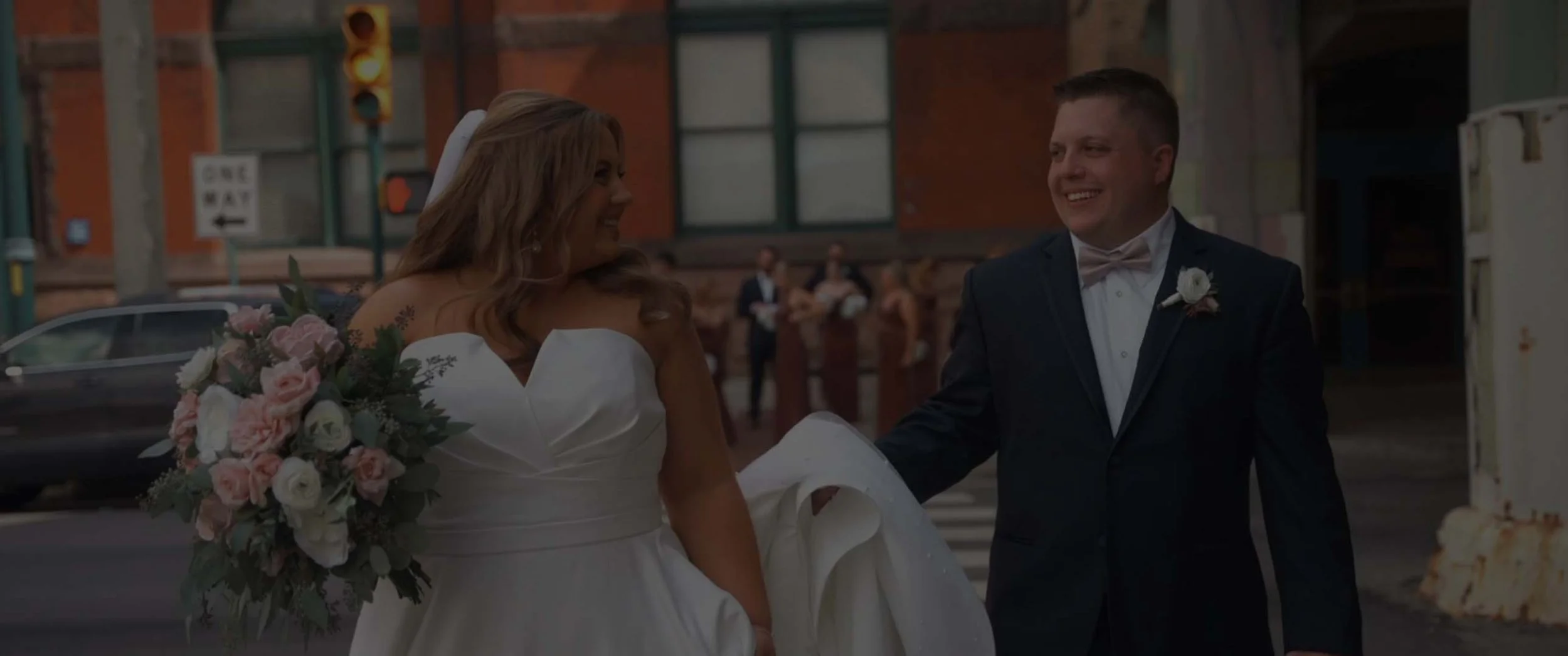 A smiling bride in a white wedding dress and a smiling groom in a tuxedo holding hands during their wedding ceremony outside a brick building. Wedding at Grand Hall at Union Station