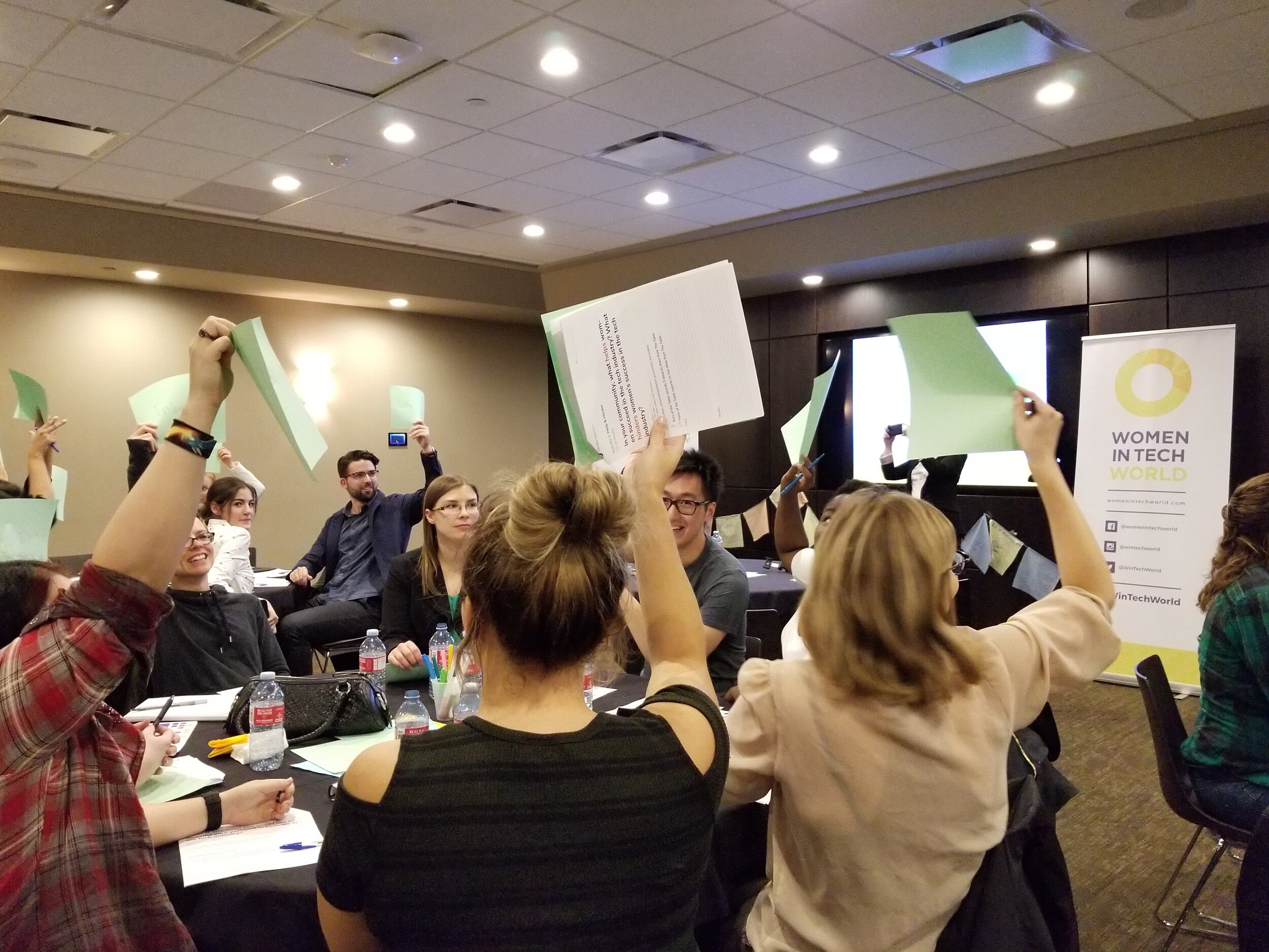  Community Conversation participants holding up green and white pieces of paper sharing their ideas. 