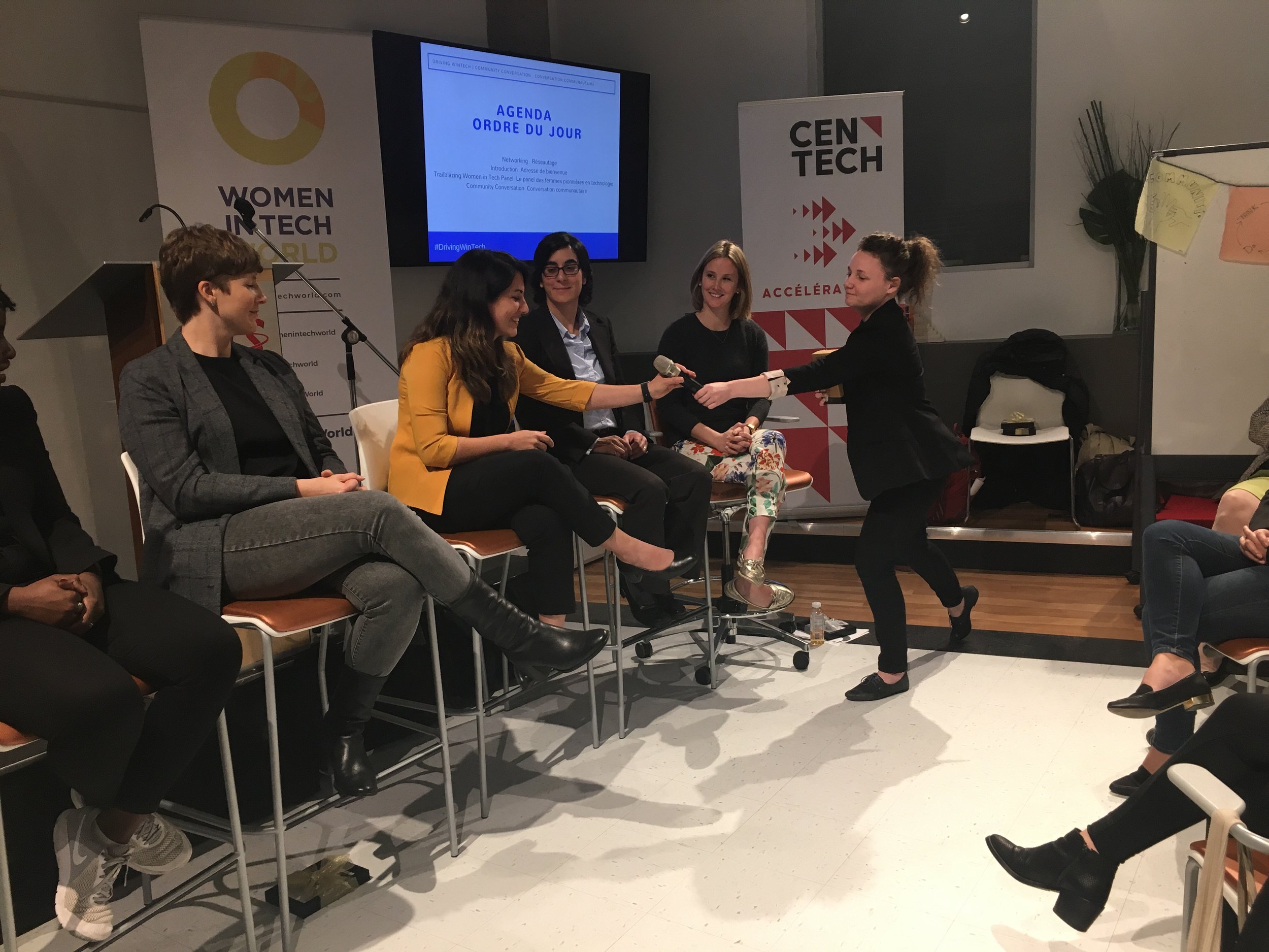  Image is of the panel in Montreal. There are five people sitting in chairs and Ali, our CEO is handing the mic to the person sitting in the middle.  