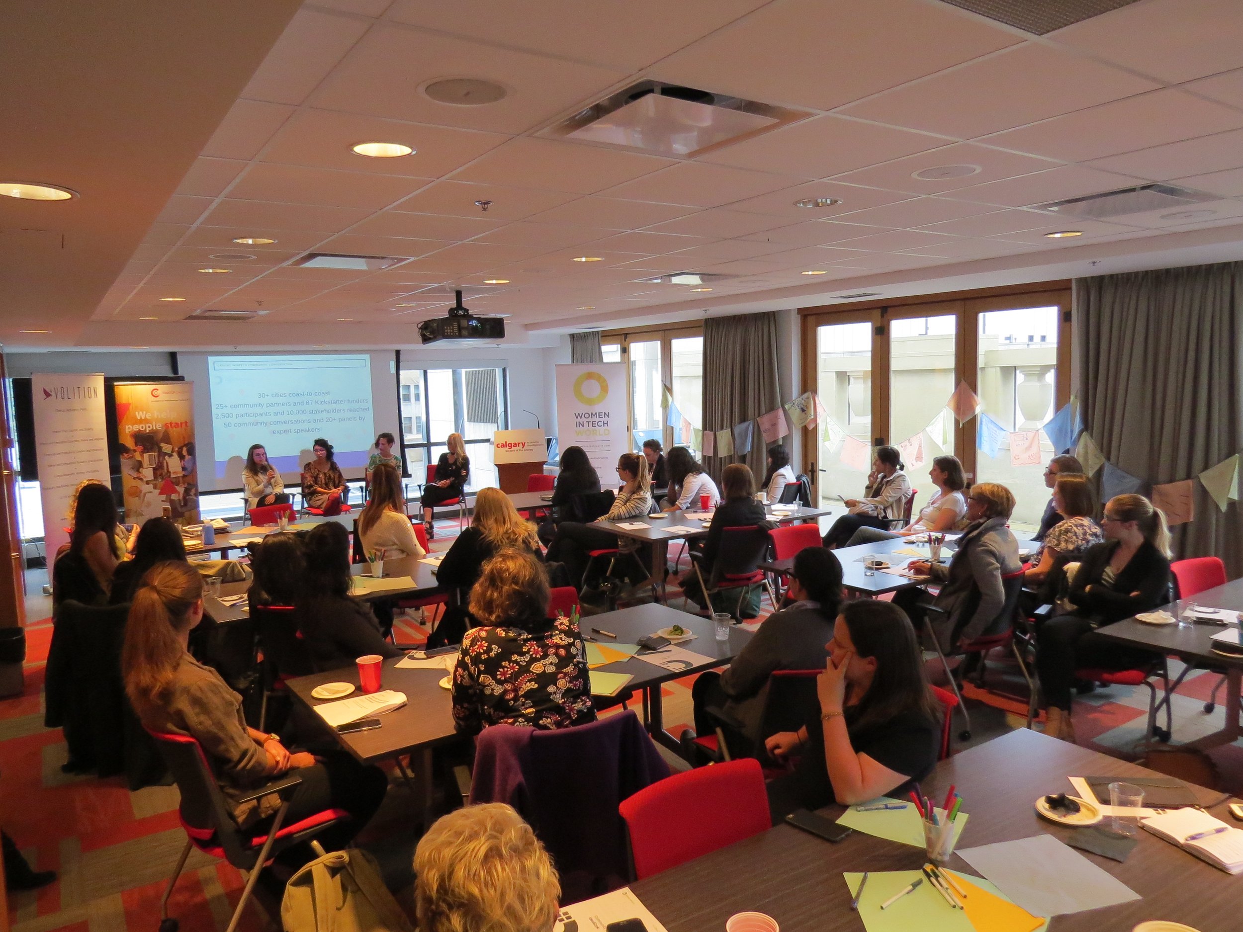  Image is of the audience looking ahead at the panelists speaking at the Community Conversation in Calgary. The room is full with people sitting at tables. 