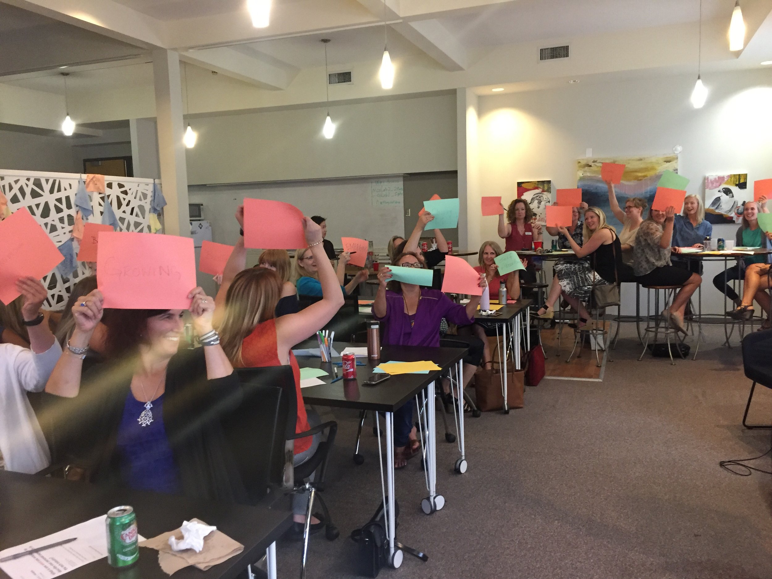  The audience for the Community Conversation in Kelowna holds up pink and blue sheets of paper with their ideas written on them. 