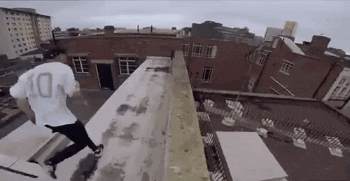 GIF of two young men performing parkour across rooftops, with the image slowing down as leap over a large gap.