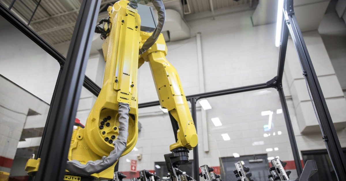 A yellow metal arm is sitting on a table. The arm is folded, creating and upside down V shape.