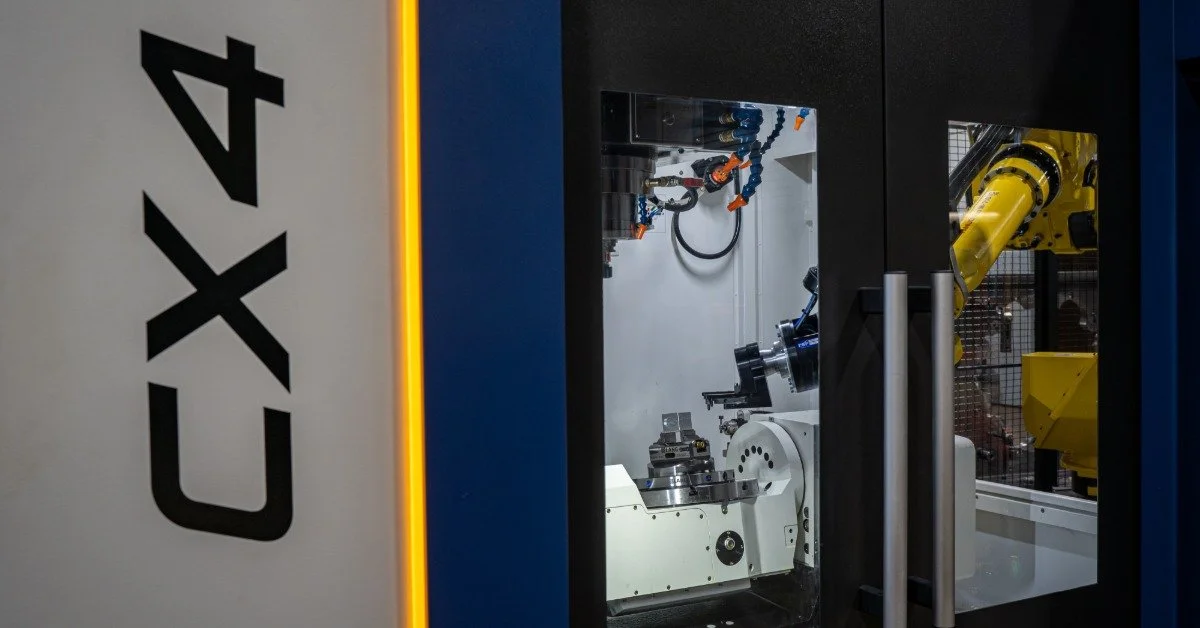 A view through a windowed door of an automated CNC machine. The machine has the characters "CX4" printed on it.