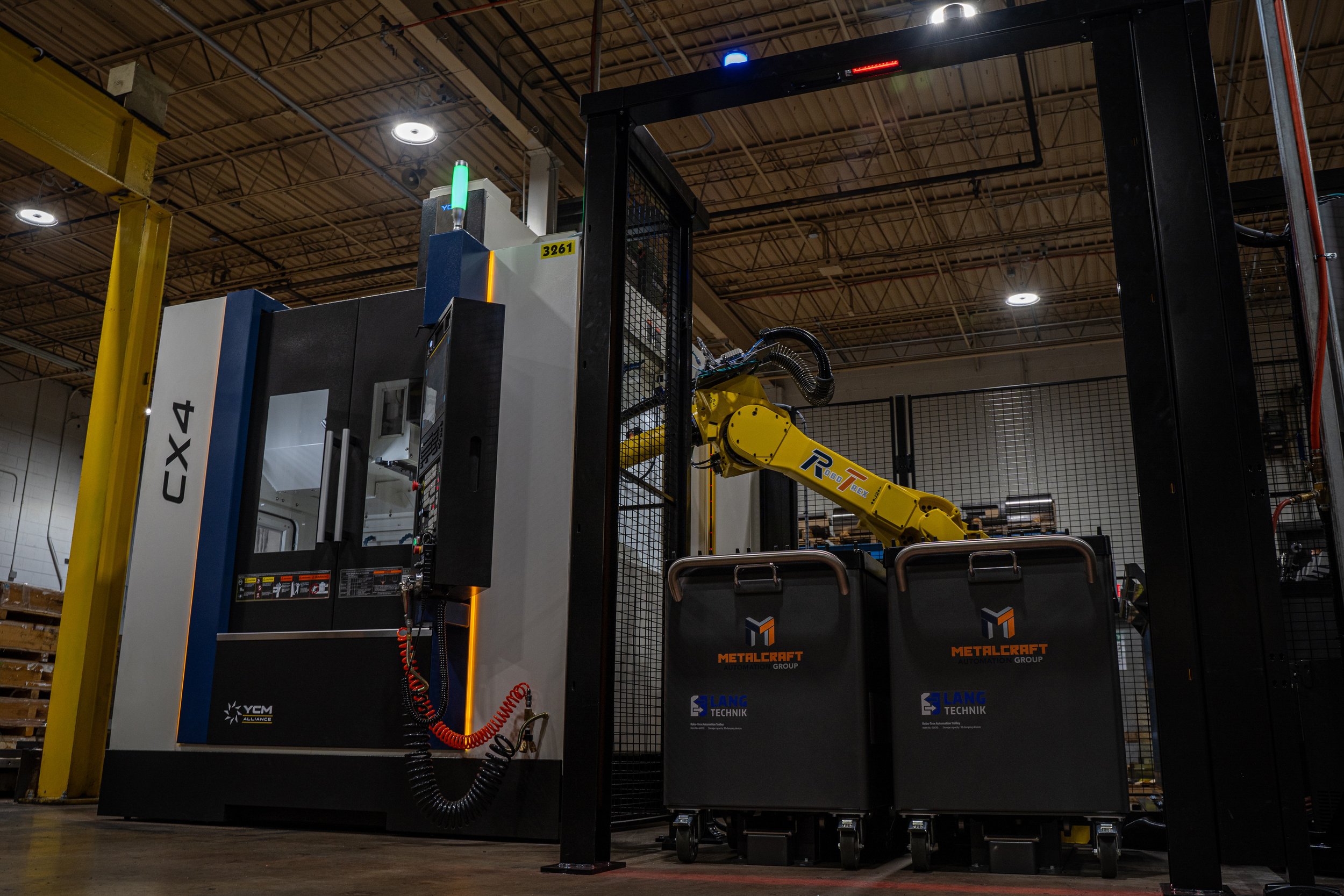A very large robotic arm, painted a yellow color, working on something inside of a walled off automation unit.