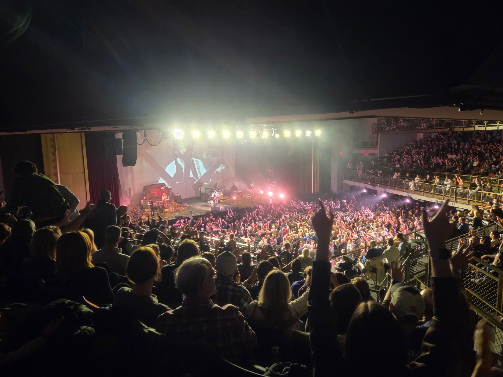 A packed MGM Music Hall at Fenway during Shaboozey's concert in Boston, viewed from an upper balcony with the stage, floor crowd and surrounding balconies visible.
