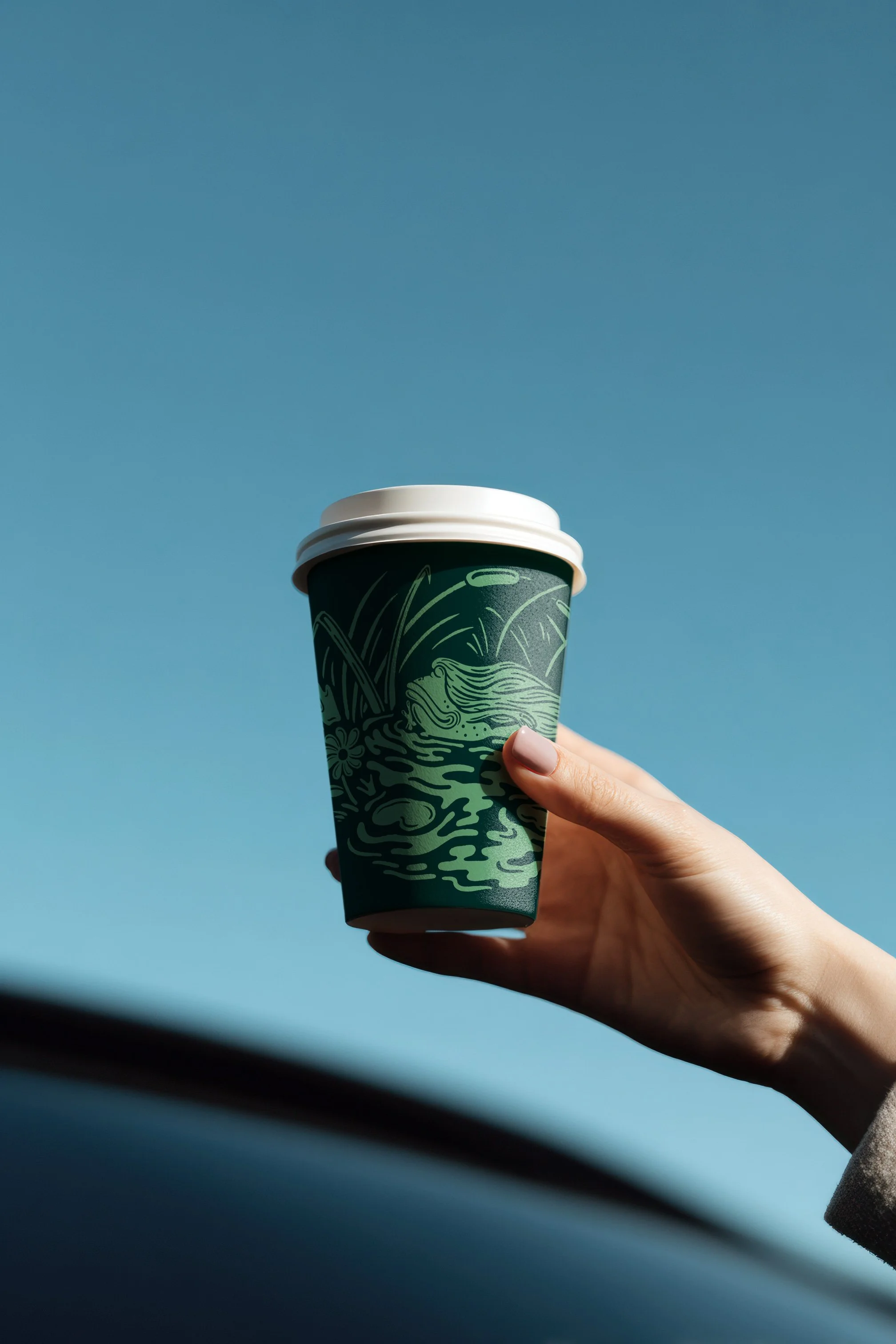 A hand holding a green coffee cup with white lid against a clear blue sky.