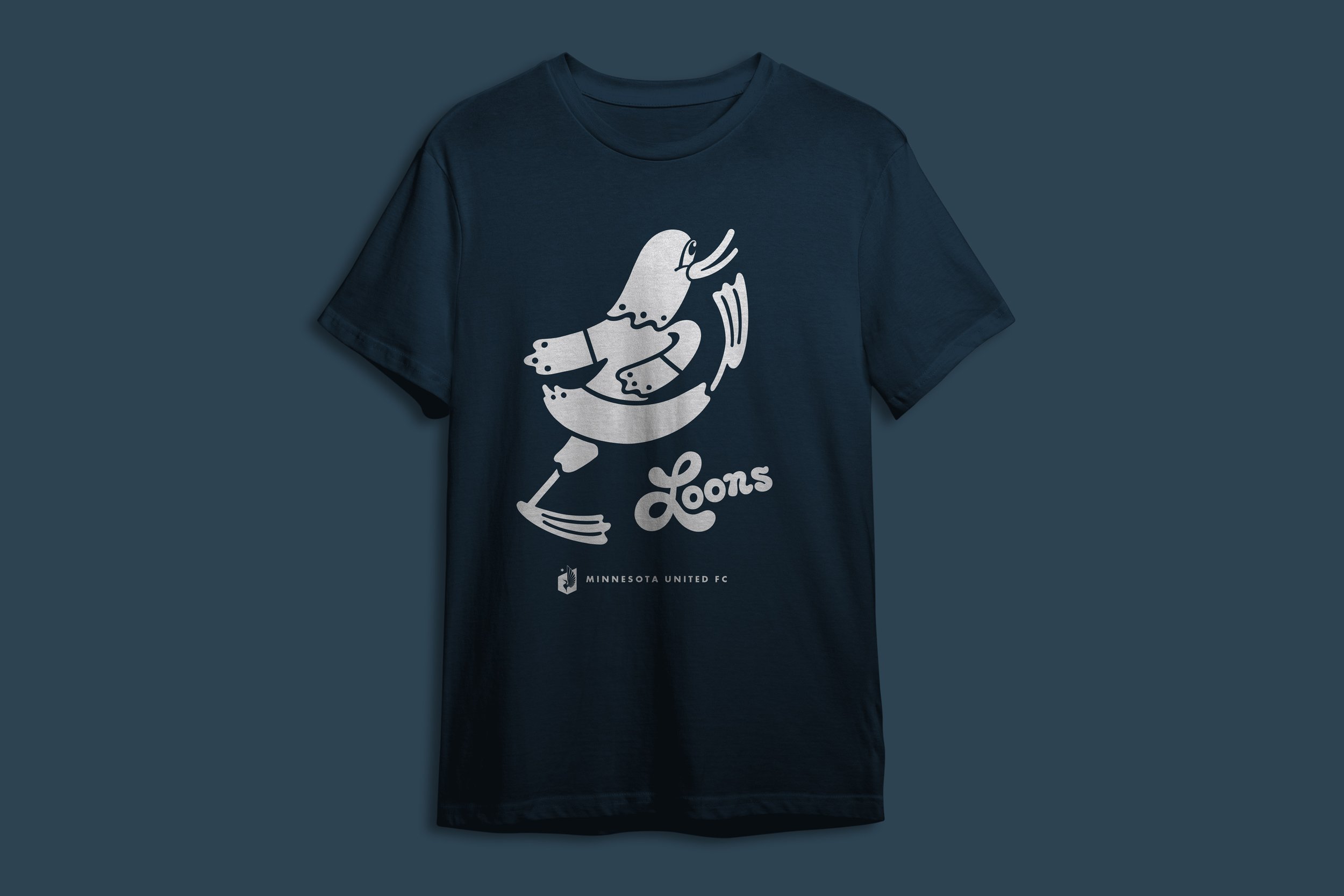 Dark blue T-shirt with a white graphic of a cartoon bird wearing a scarf, holding a hockey stick, and the text 'Loons' underneath, representing Minnesota United FC.