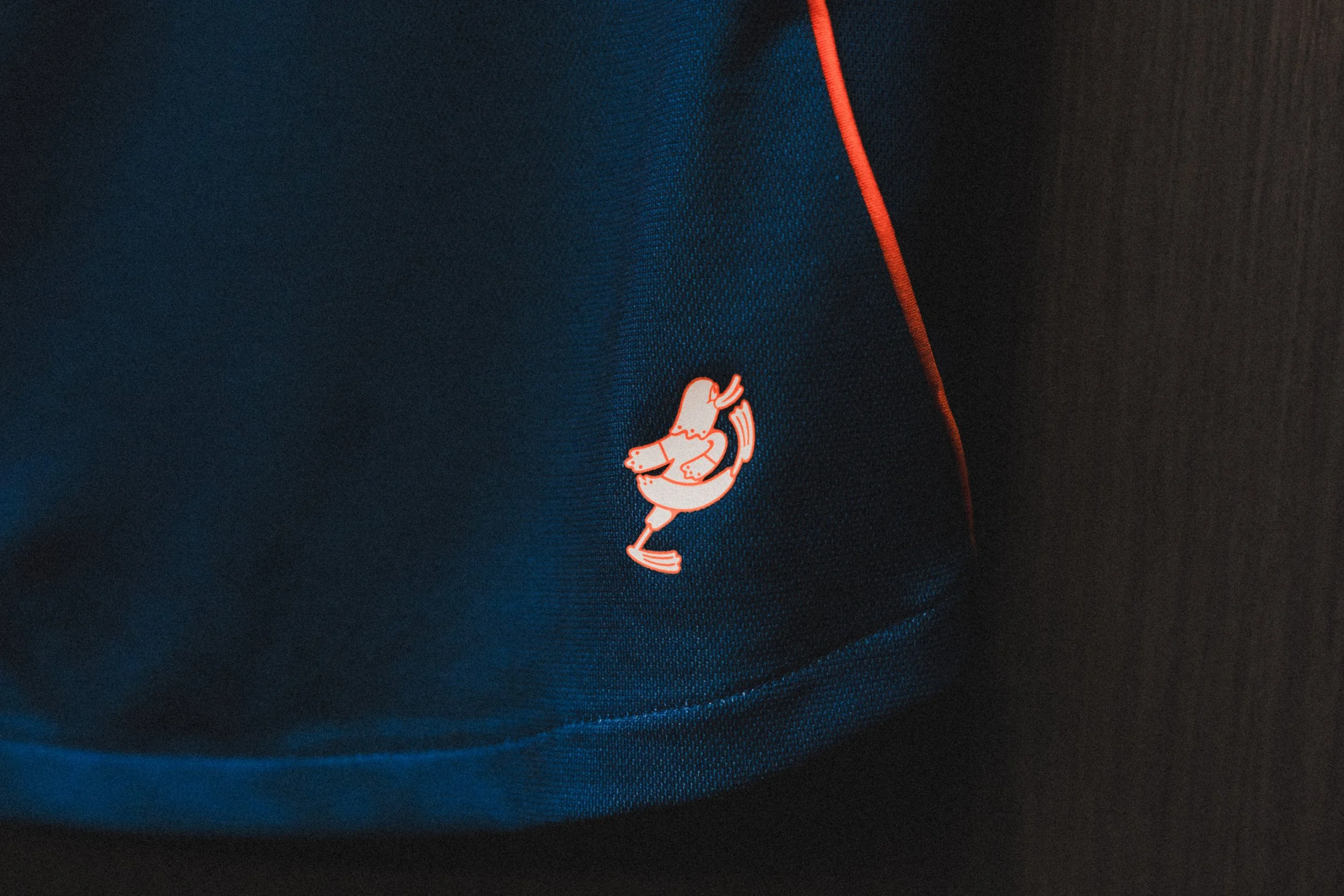 Close-up of a blue soccer jersey with orange piping and a small cartoon loon logo in white and orange.