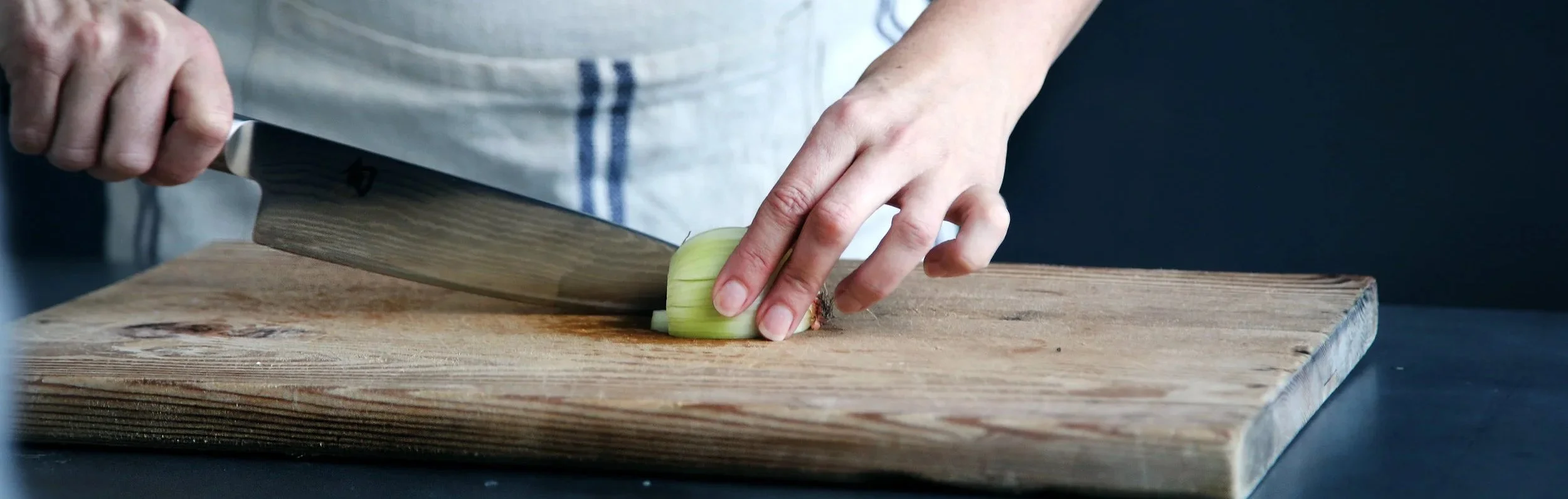 Person chopping a green onion on a wooden cutting board with a knife. Do you have the skills to work here?