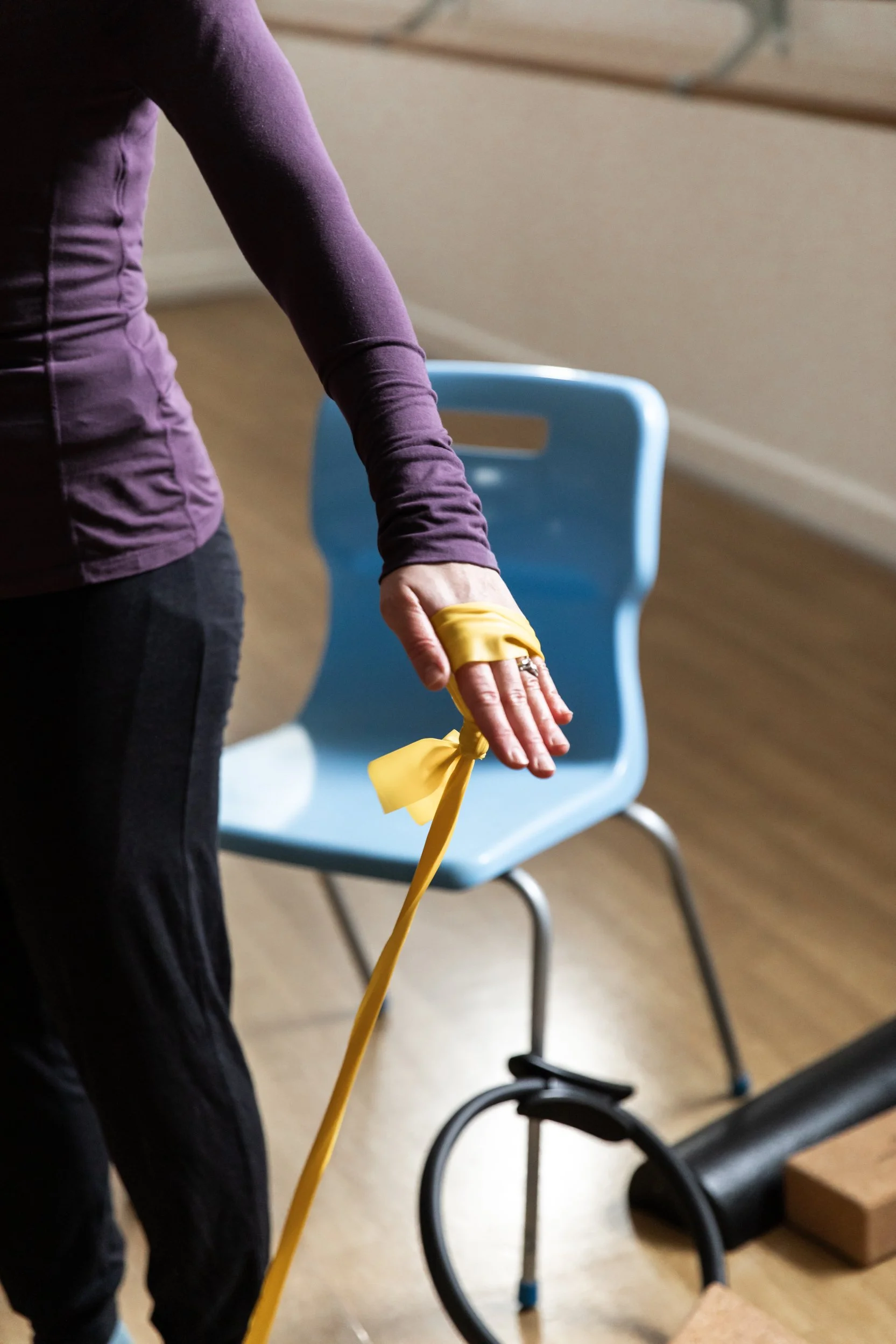 Two elderly women and a younger woman doing stretching exercises outdoors during the daytime. The women are sitting on chairs, and the younger woman is standing between them, all in a relaxed pose.