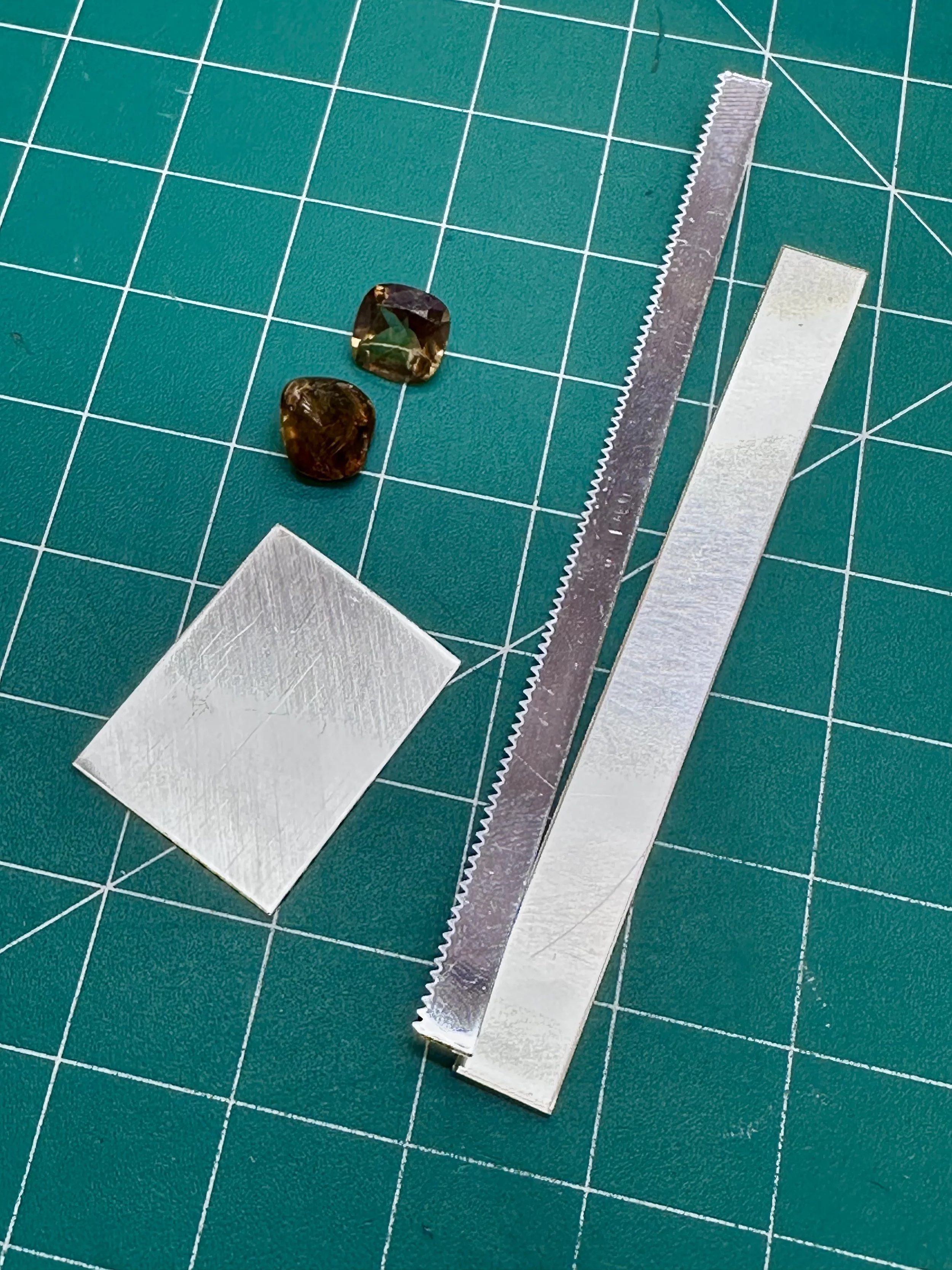 Tourmaline gemstones and silver sheet laid out on a workbench during a jewelry making class in Albuquerque