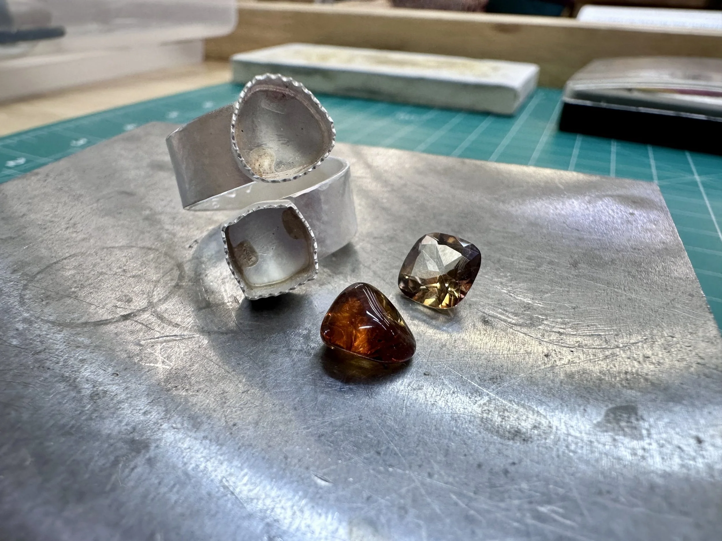 Multiple handmade tourmaline wrap rings on a metal surface during a jewelry workshop in Albuquerque