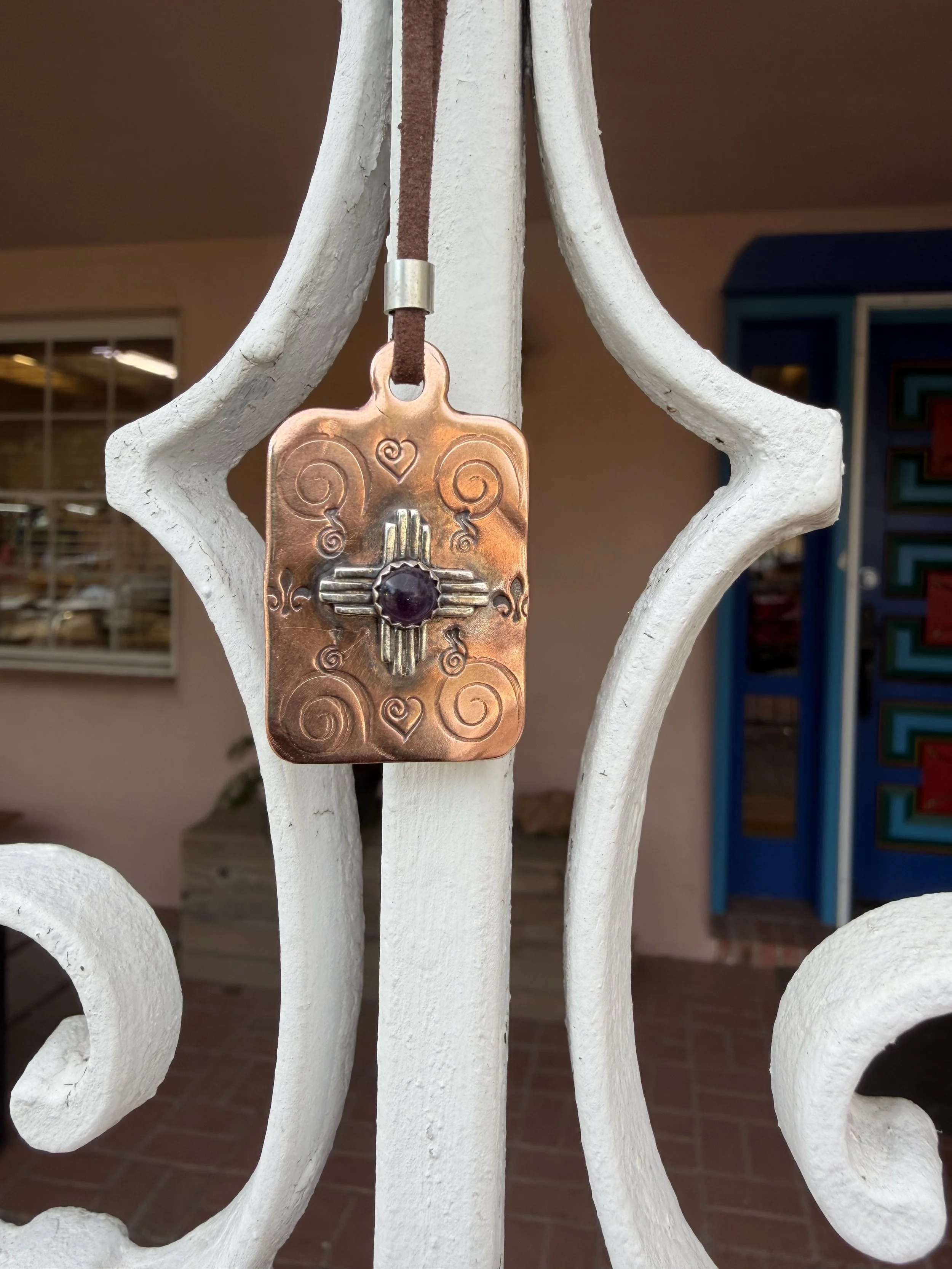 Stamped Zia necklace hanging on display showing texture and detail from a jewelry making class in Albuquerque.
