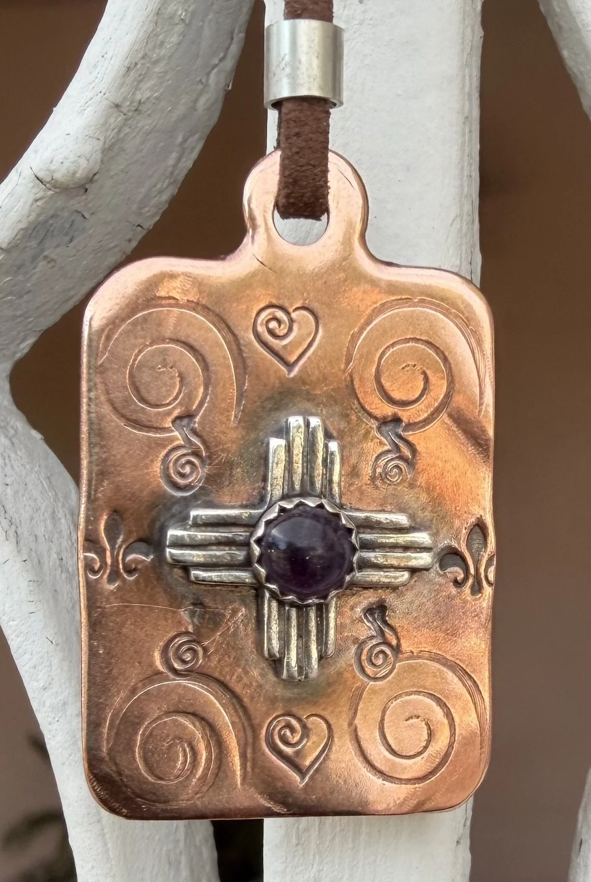 Close up of copper Zia pendant with turquoise cabochon created in a jewelry making class in Albuquerque