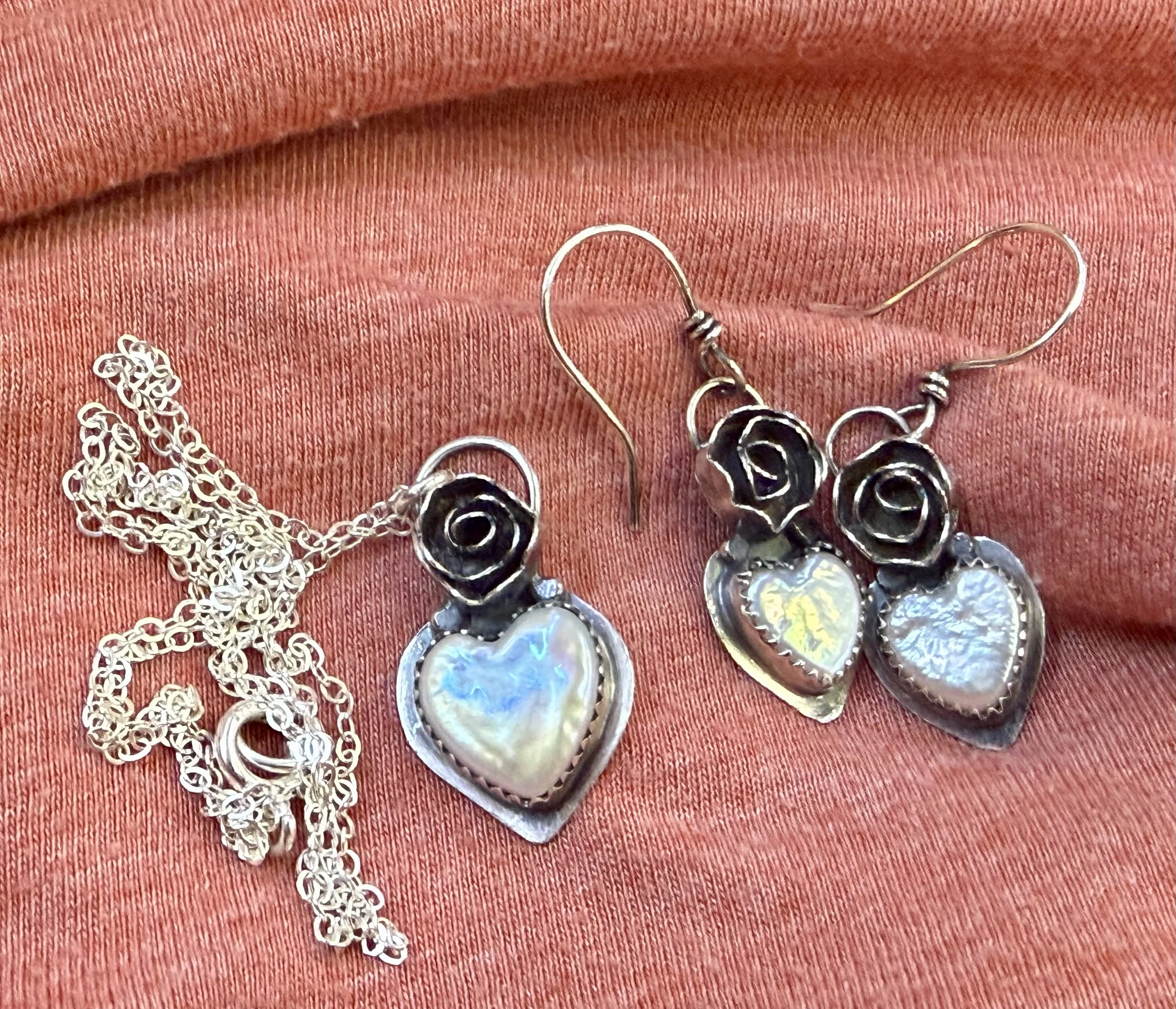 Handmade sterling silver blooming heart earrings with pearl drops displayed on fabric after a jewelry workshop in Albuquerque