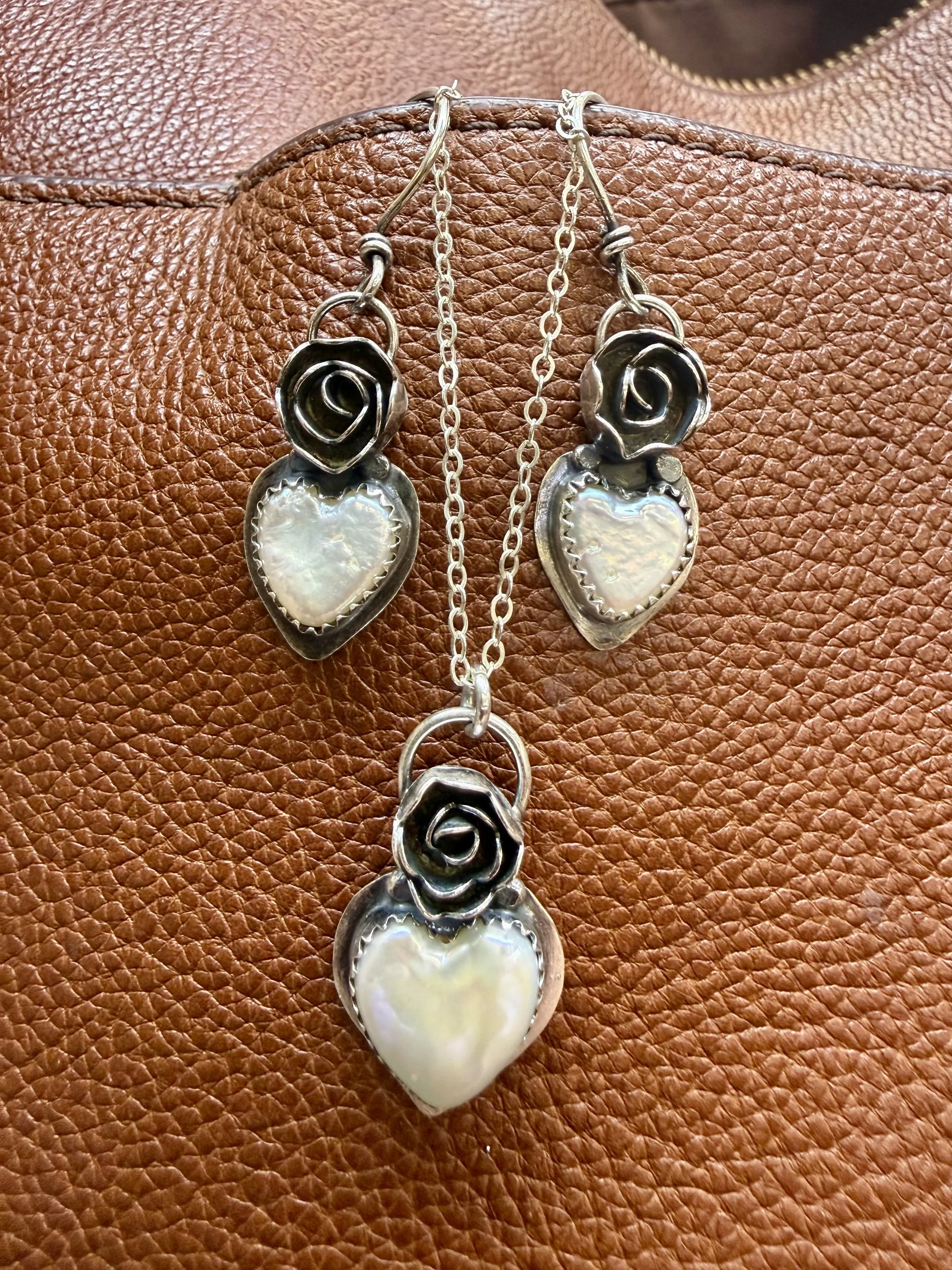 Sterling silver blooming heart earrings with pearl drops on leather background created in a jewelry workshop in Albuquerque